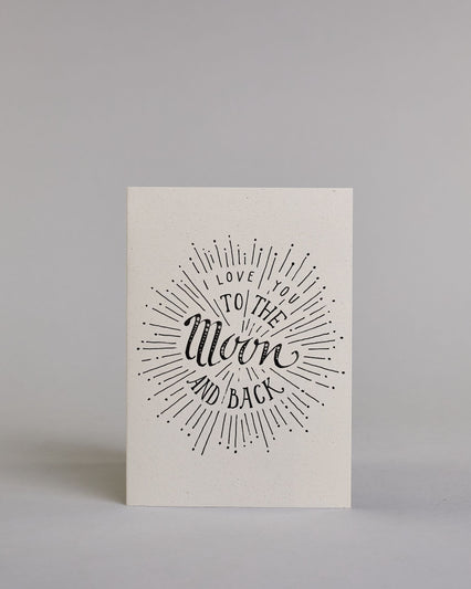 Klappkarte für Liebende auf Englisch mit schwarzer Kalligrafieaufschrift "I love you to the moon and back" auf hellem Hintergrund. Der Text ist in folgende vier Zeilen aufgeteilt: "I lOVE YOU" in dünner gerader Kalligrafieschrift, darunter "TO THE" in größerer gerader Kalligrafieschrift, darunter "Moon" in kunstvoller Schreibschrift, darunter "AND BACK" and verspielter gerader Kalligrafieschrift. Der Text ist umgeben von einzelnen Linien und Punkten die im Gesamtbild einen Kreis, ähnlich einer Explosion, e…