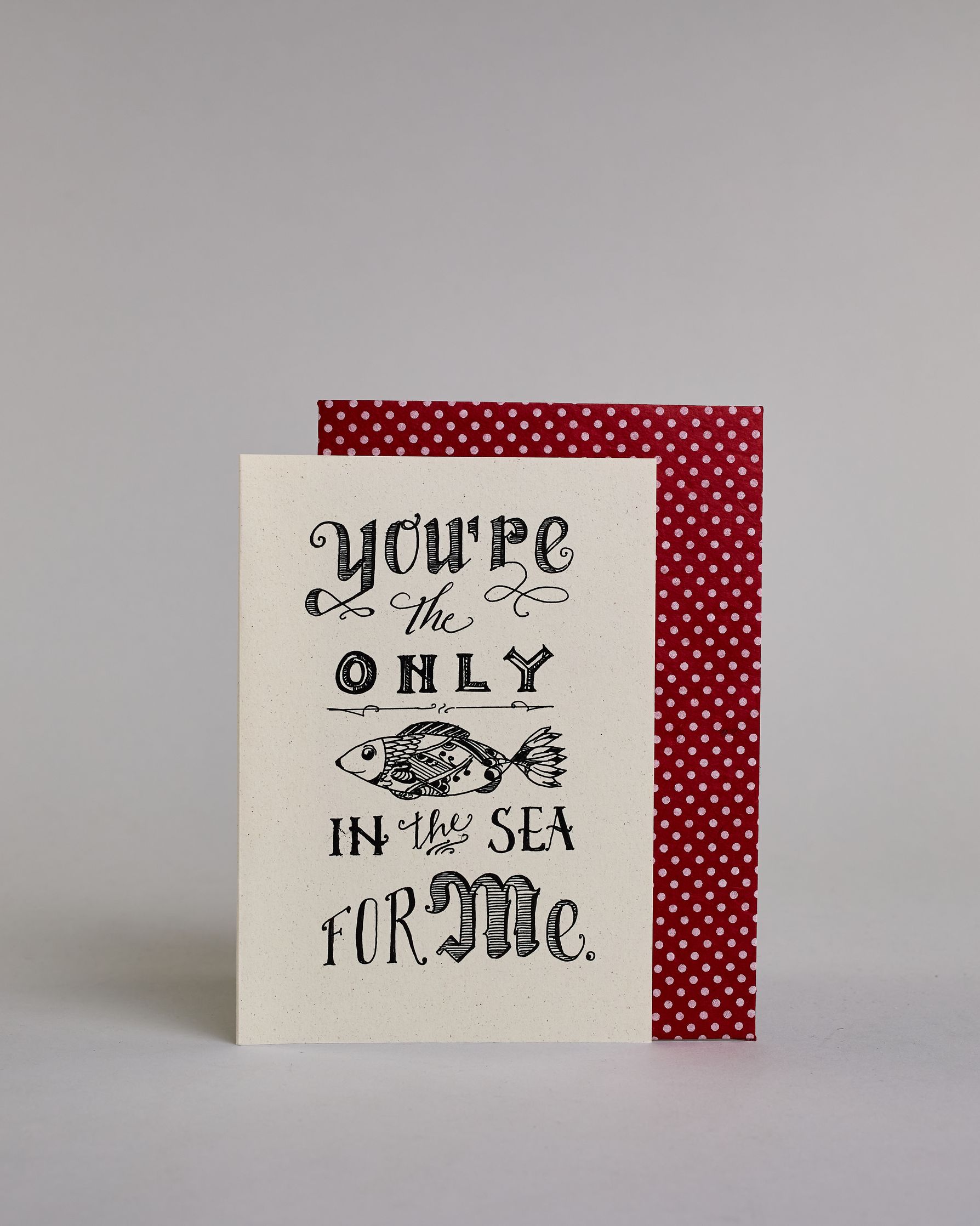 Klappkarte für Liebende auf Englisch mit schwarzer Kalligrafieaufschrift "you're the only fish in the sea for me" mit einem gezeichneten Fisch auf hellem Hintergrund. Der Text ist in folgende fünf Zeilen aufgeteilt: "you're" in geschwungener kunstvoller Kalligrafieschrift, darunter "the" in dünner Schreibschrift zwischen zwei Schnörkeln, darunter "ONLY" in kunstvoller Kalligrafieschrift, darunter eine horizontale Linie, darunter ein kunstvoll gestalteter gezeichneter Fisch, darunter "IN the SEA" in verspie…