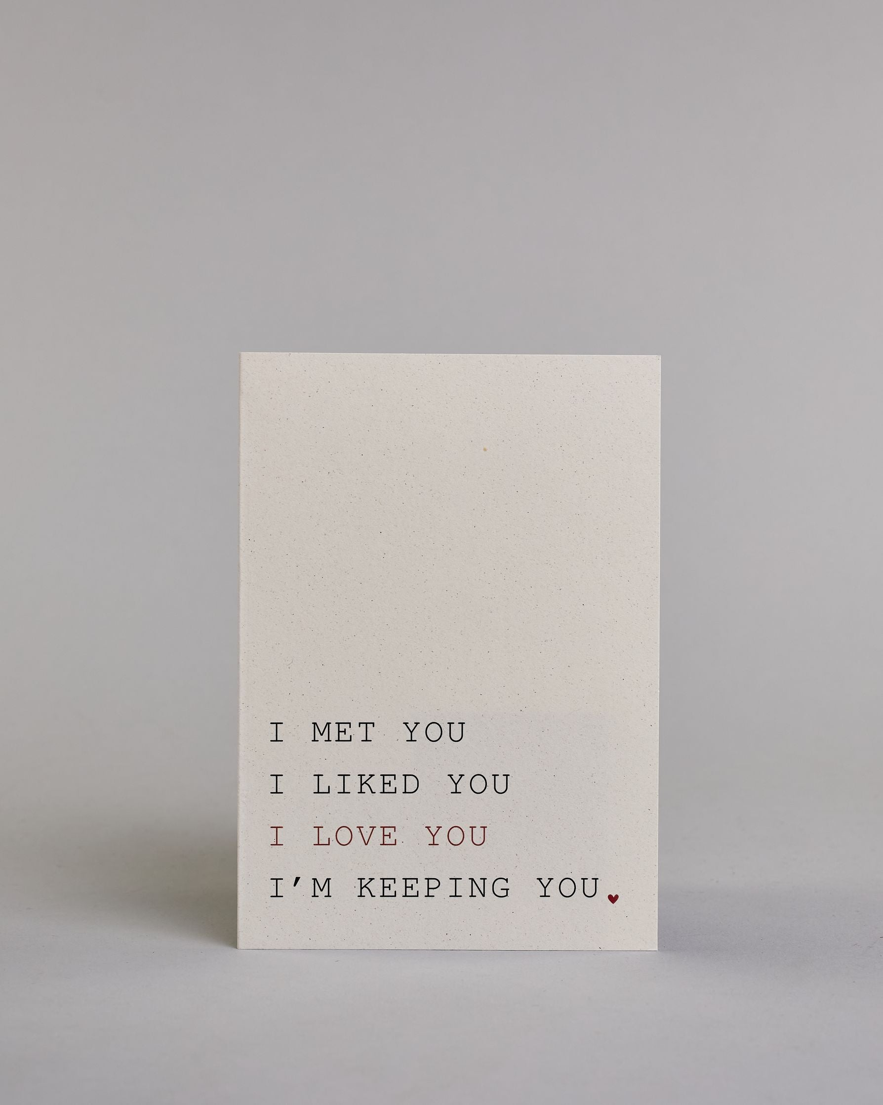 Klappkarte für Liebende auf Englisch mit schwarzer und roter Kalligrafieaufschrift "I met you I liked you I love you I'm keeping you." auf hellem Hintergrund. Der Text ist in folgende vier Zeilen aufgeteilt: "I MET YOU" in schwarzer, darunter "I LIKED YOU" in schwarzer, darunter "I LOVE YOU" in roter, darunter "I'M KEEPING YOU." in schwarzer Schrift, der Punkt hinter dem "YOU" ist ein kleines rotes Herz. Alle Zeile sind in einer Kalligrafieschrit gestaltet die an die tyische Schreibmaschinenschrift erinner…