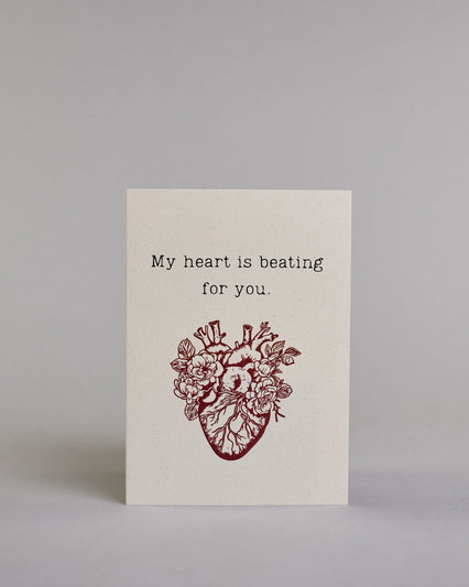 Klappkarte für Liebende auf Englisch mit schwarzer und Kalligrafieaufschrift "My heart is beating for you." mit einem rotem gezeichnetem Herz das einem echten Herz nachempfunden ist, allerdings ist es mit Blüten und Blättern verschönert auf hellem Hintergrund. Der Text ist in folgende zwei Zeilen aufgeteilt: "My heart is beating", darunter "for you." - beide Zeile in typischer Schreibmaschinenschrift, darunter das rote Herz. Dazu ein rot-weißes handgeschöpftes Kuvert. #1