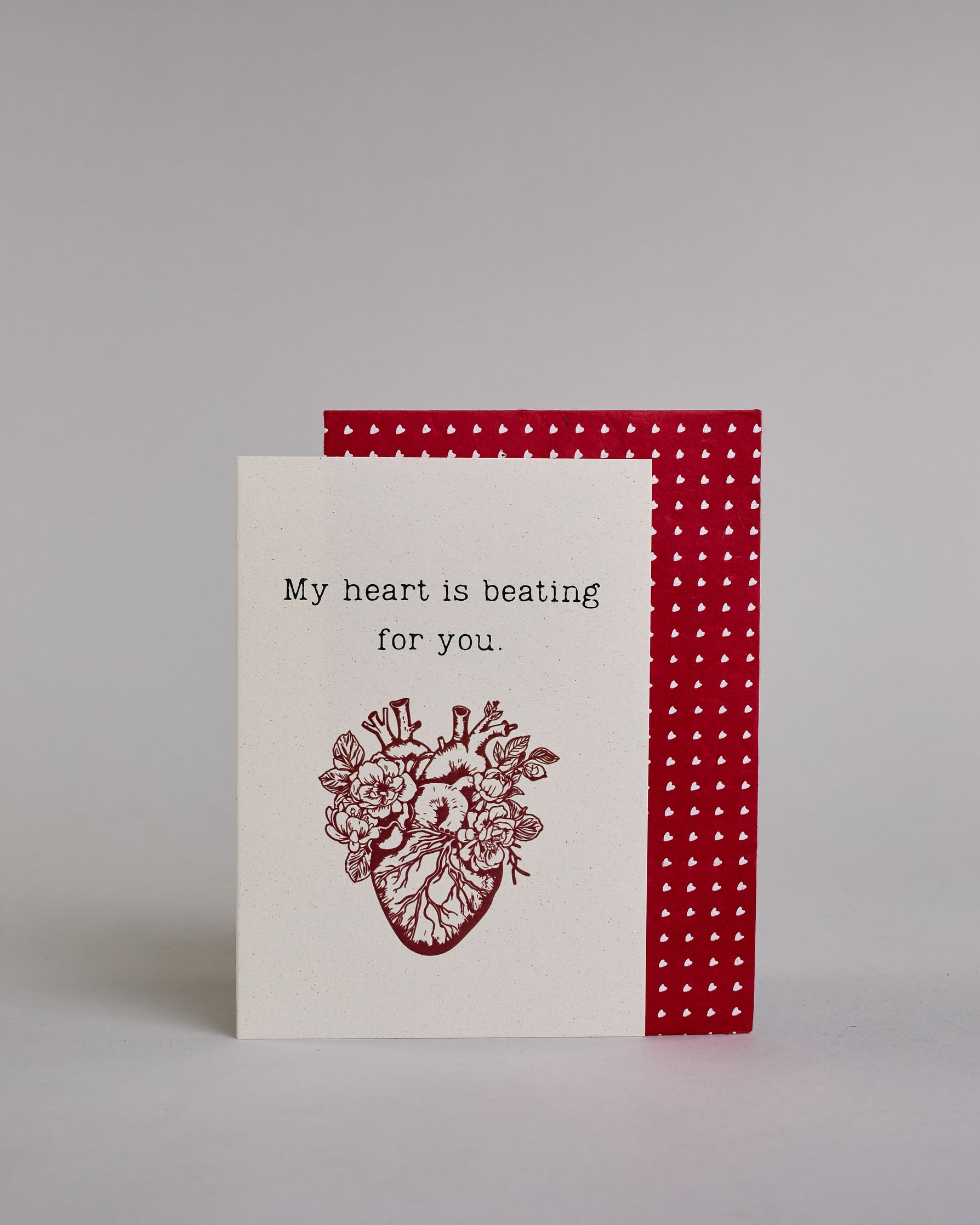 Klappkarte für Liebende auf Englisch mit schwarzer und Kalligrafieaufschrift "My heart is beating for you." mit einem rotem gezeichnetem Herz das einem echten Herz nachempfunden ist, allerdings ist es mit Blüten und Blättern verschönert auf hellem Hintergrund. Der Text ist in folgende zwei Zeilen aufgeteilt: "My heart is beating", darunter "for you." - beide Zeile in typischer Schreibmaschinenschrift, darunter das rote Herz. Dazu ein rot-weißes handgeschöpftes Kuvert. #2