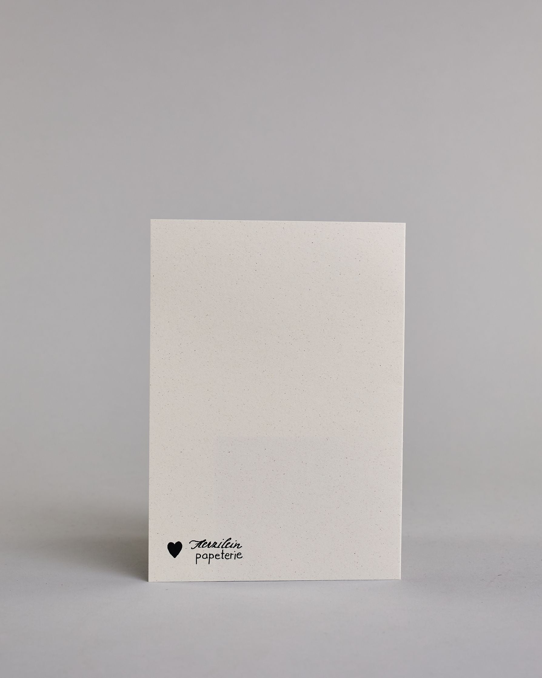 Klappkarte für Liebende auf Englisch mit schwarzer Kalligrafieaufschrift "Everybunny needs somebunny sometimes", darunter sind zwei gezeichnete Hasen in einem hellen beige und hellem grau die ihre Nasen aufeinander zuführen auf hellem Hintergrund. Der rechte Hase hat eine rote Masche um den Hals und über ihren Köpfen ist ein rotes Herz. Die Kalligrafieschrift ist dünn und gerade und teilt sich in zwei Zeilen mit jeweils immer zwei Worten auf. Die Schrift ist im oberen linken Teil der Karte, während die Has…