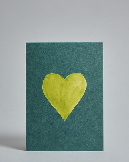 Die Vorderseite der Postkarte im Hochformat vor hellgrauem Hintergrund. Die Postkarte zeigt ein grünes, gezeichnet aussehendes Herz auf mintfarbenem Hintergrund gedruckt auf Holzschliffpappe.