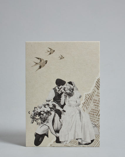 Die Vorderseite der Postkarte im Hochformat vor hellgrauem Hintergrund. Die Postkarte ist im Retro-Stil, gedruckt auf Holzschiffpappe. Im Vordergrund ist ein Hochzeitspaar auf einem Moped geschmückt mit Blumen in Graustufen. Im Hintergrund sind Zeitungsschnippsel und Papier zu sehen.