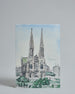 Die Vorderseite der Postkarte im Hochformat, gedruckt auf hochwertigem Papier. Diese zeigt die Wiener Votivkirche vor blauem Himmel gemalt von einer Wiener Künstlerin. Im unteren Teil der Karte ist ein Teil des Votivkparks zu sehen. rechts neben der Kirche auf mittlerer Höhe ist "Vienna" in dezenter, geschwungener Schrift zu lesen.