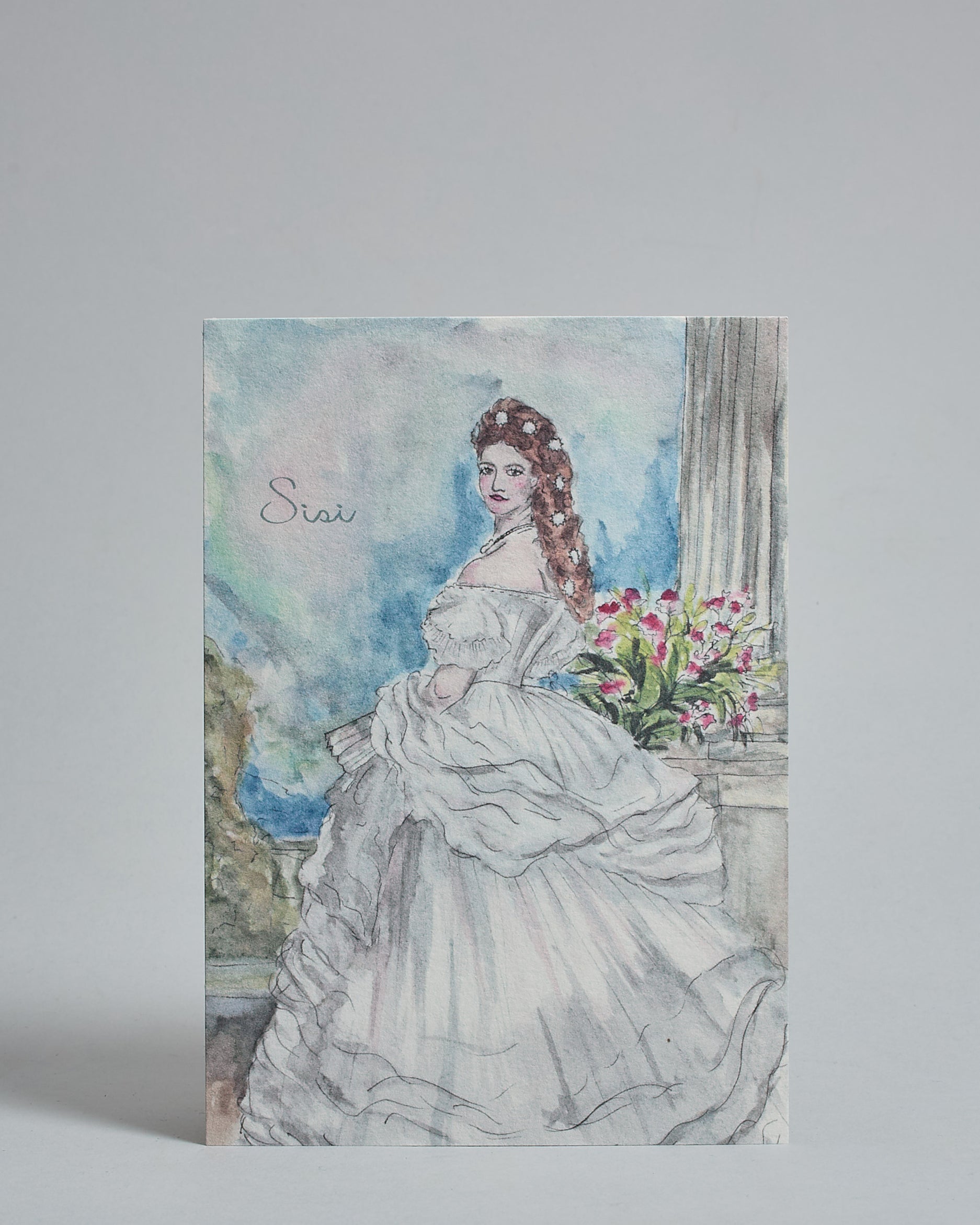 Die Vorderseite der Postkarte im Hochformat, gedruckt auf hochwertigem Papier. Diese zeigt die Kaiserin Sisi gemalt von einer Wiener Künstlerin. Auf der linken Seite ist "Sisi" in dezenter, geschwungener Schrift zu lesen.