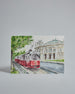 Die Vorderseite der Postkarte im Querformat, gedruckt auf hochwertigem Papier. Diese zeigt eine alte Wiener Straßenbahn vor dem Burgtheater gemalt von einer Wiener Künstlerin. Anstelle von Fahrziel und Liniennummer sind ein Herz und "Herzilein" auf der Straßenbahn zu lesen. Im linken Bildteil ist ein Baum, dessen grüne Krone teilweise über die Straßenbahn reicht.