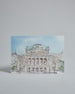 Die Vorderseite der Postkarte im Querformat, gedruckt auf hochwertigem Papier. Diese zeigt die Wiener Staatsoper vor blauem Himmel gemalt von einer Wiener Künstlerin. Links neben dem Gebäude ist der Schriftzug "Vienna" in dezenter, geschwungener Schrift zu lesen.