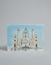 Die Vorderseite der Postkarte im Querformat, gedruckt auf hochwertigem Papier. Diese zeigt die Wiener Karlskirche vor blauem Himmel gemalt von einer Wiener Künstlerin. Im unteren Teil der Karte ist ein Brunnen zu sehen in dem sich die Kirche spiegelt.
Rechts neben der Kirche ist "Wien" in dezenter, geschwungener Schrift zu lesen.