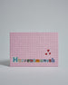 Die Vorderseite der Postkarte im Querformat vor hellgrauem Hintergrund. Im Vordergrund der Postkarte steht "Herzensmensch" in Buchstaben die aussehen als wären sie aus Zeitrschriften ausgeschnitten. Der Hintergrund ist rosa mit dezentem Karomuster.