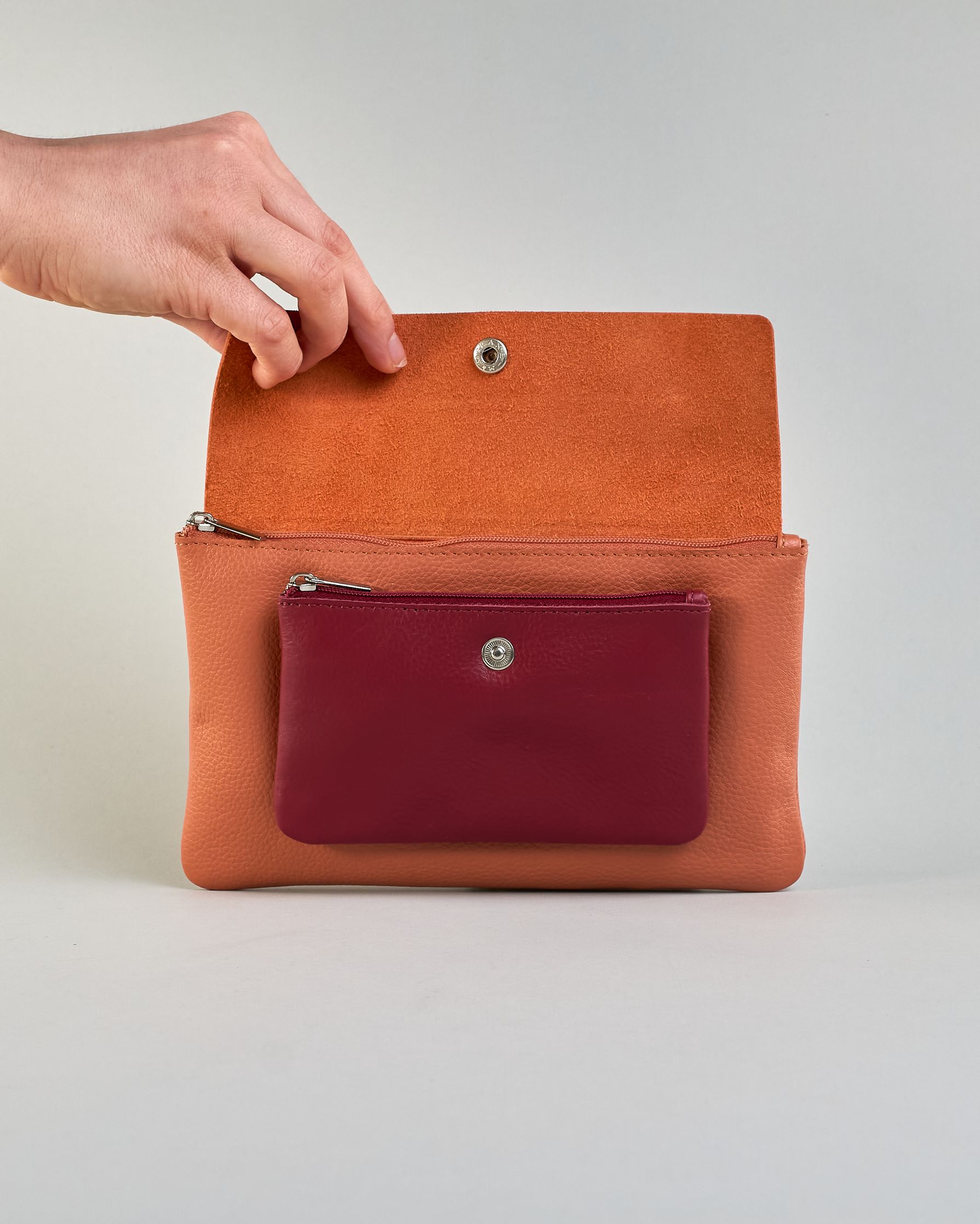 Kosmetiktasche aus Leder mit einem großen orangenen Zippfach und einem kleinen roten Zippfach vorne, darüber eine orangene Lasche mit Druckknopf. #3