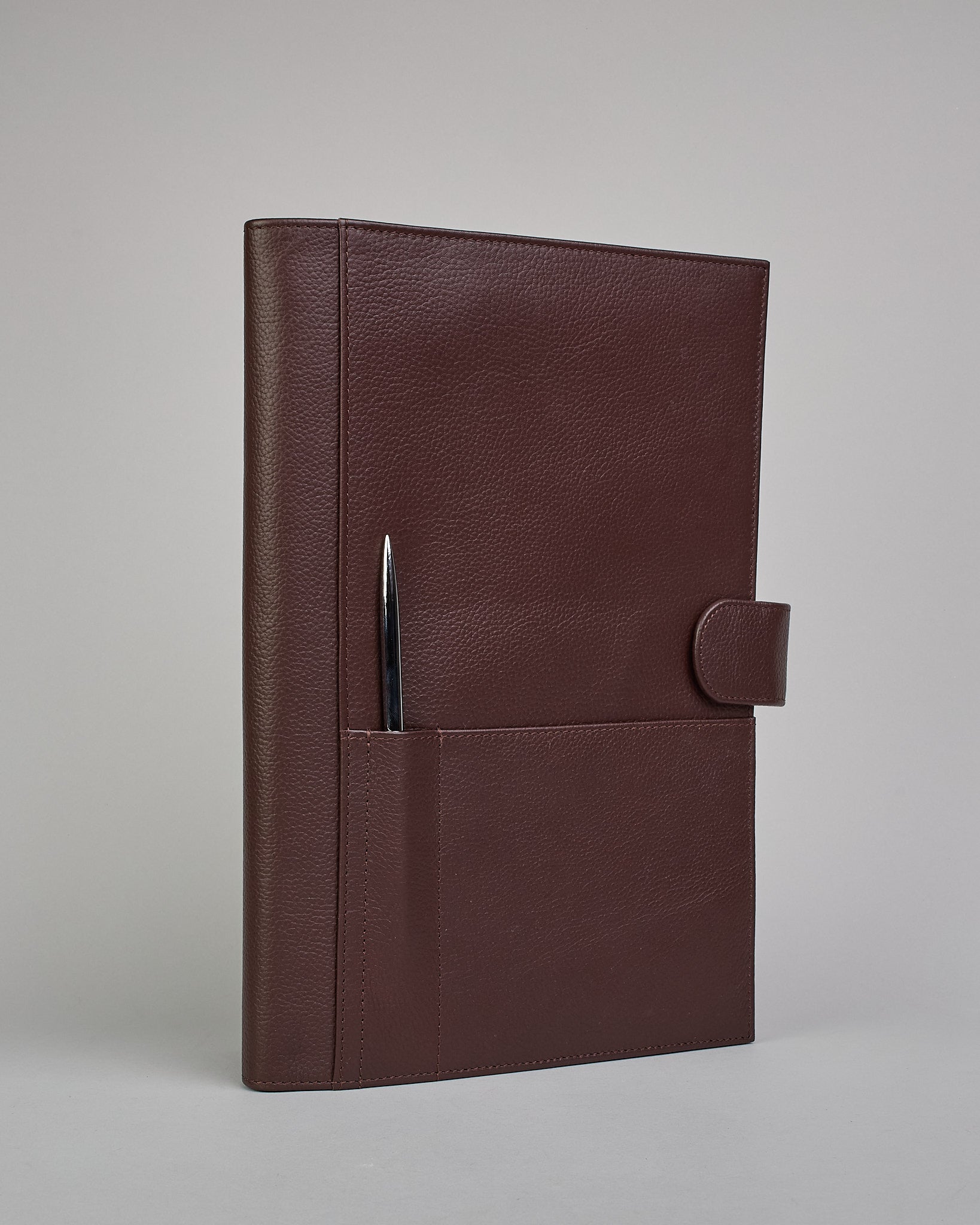 Dunkelbrauner Leder Notizbucheinband mit leichter Narbund. Der Einband hat außen ein flaches Fach in das ein Stift und das Handy gesteckt werden können. Das Notizbuch lässt sich seitlich mit einer Lasche und einem darunterliegenden Druckknopf verschließen. Innen bietet das Notizbuch rechts Platz um ein Buch einzustecken und links gibt es viele Fächer für weitere Notizzettel, Visitkarten und mehr. #1