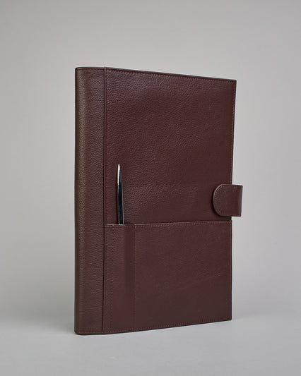 Dunkelbrauner Leder Notizbucheinband mit leichter Narbund. Der Einband hat außen ein flaches Fach in das ein Stift und das Handy gesteckt werden können. Das Notizbuch lässt sich seitlich mit einer Lasche und einem darunterliegenden Druckknopf verschließen. Innen bietet das Notizbuch rechts Platz um ein Buch einzustecken und links gibt es viele Fächer für weitere Notizzettel, Visitkarten und mehr. #1