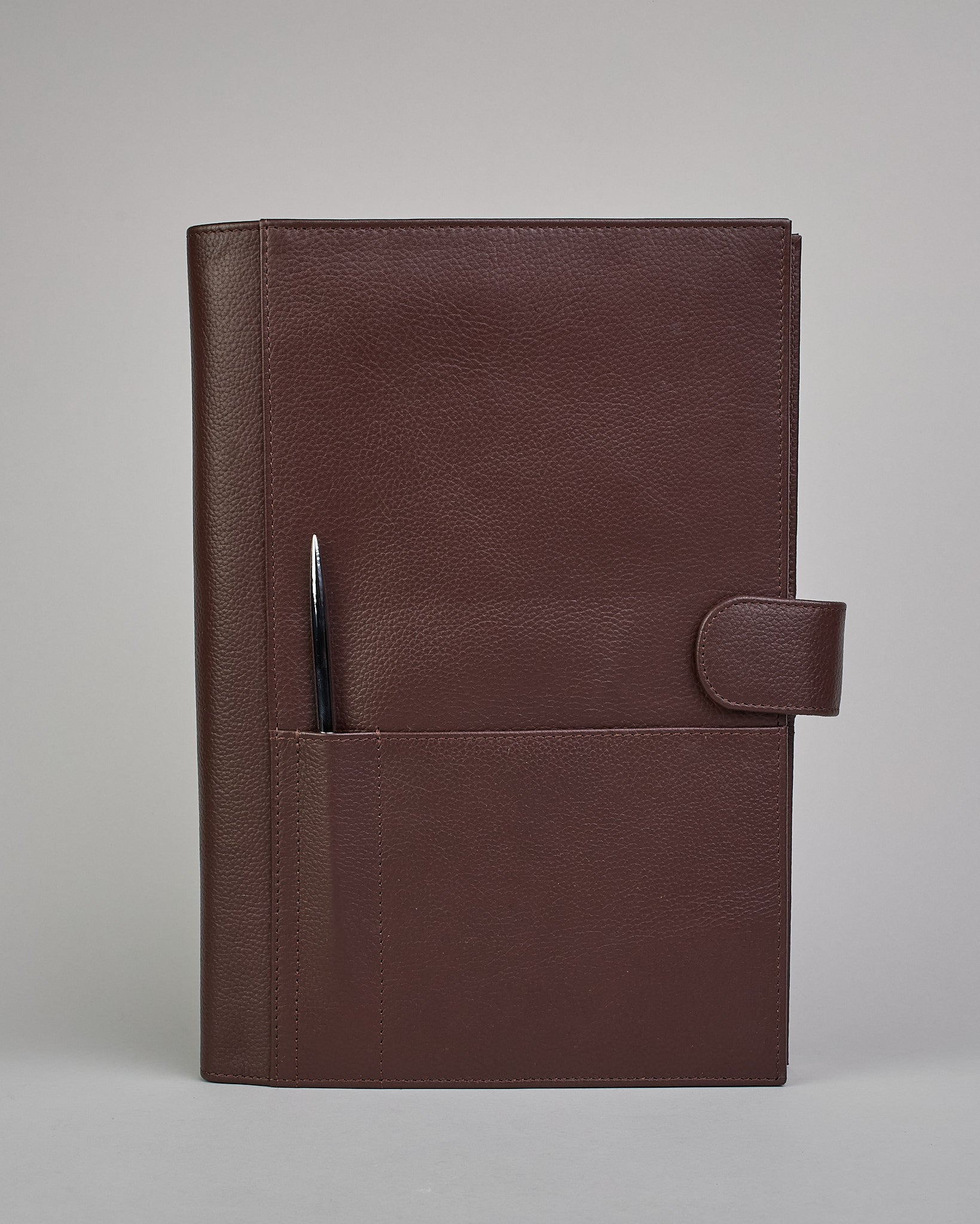 Dunkelbrauner Leder Notizbucheinband mit leichter Narbund. Der Einband hat außen ein flaches Fach in das ein Stift und das Handy gesteckt werden können. Das Notizbuch lässt sich seitlich mit einer Lasche und einem darunterliegenden Druckknopf verschließen. Innen bietet das Notizbuch rechts Platz um ein Buch einzustecken und links gibt es viele Fächer für weitere Notizzettel, Visitkarten und mehr. #2