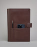 Dunkelbrauner Leder Notizbucheinband mit leichter Narbund. Der Einband hat außen ein flaches Fach in das ein Stift und das Handy gesteckt werden können. Das Notizbuch lässt sich seitlich mit einer Lasche und einem darunterliegenden Druckknopf verschließen. Innen bietet das Notizbuch rechts Platz um ein Buch einzustecken und links gibt es viele Fächer für weitere Notizzettel, Visitkarten und mehr. #4