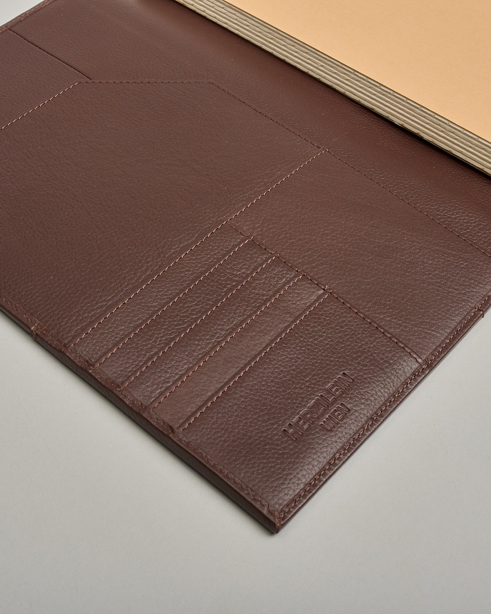 Dunkelbrauner Leder Notizbucheinband mit leichter Narbund. Der Einband hat außen ein flaches Fach in das ein Stift und das Handy gesteckt werden können. Das Notizbuch lässt sich seitlich mit einer Lasche und einem darunterliegenden Druckknopf verschließen. Innen bietet das Notizbuch rechts Platz um ein Buch einzustecken und links gibt es viele Fächer für weitere Notizzettel, Visitkarten und mehr. #5