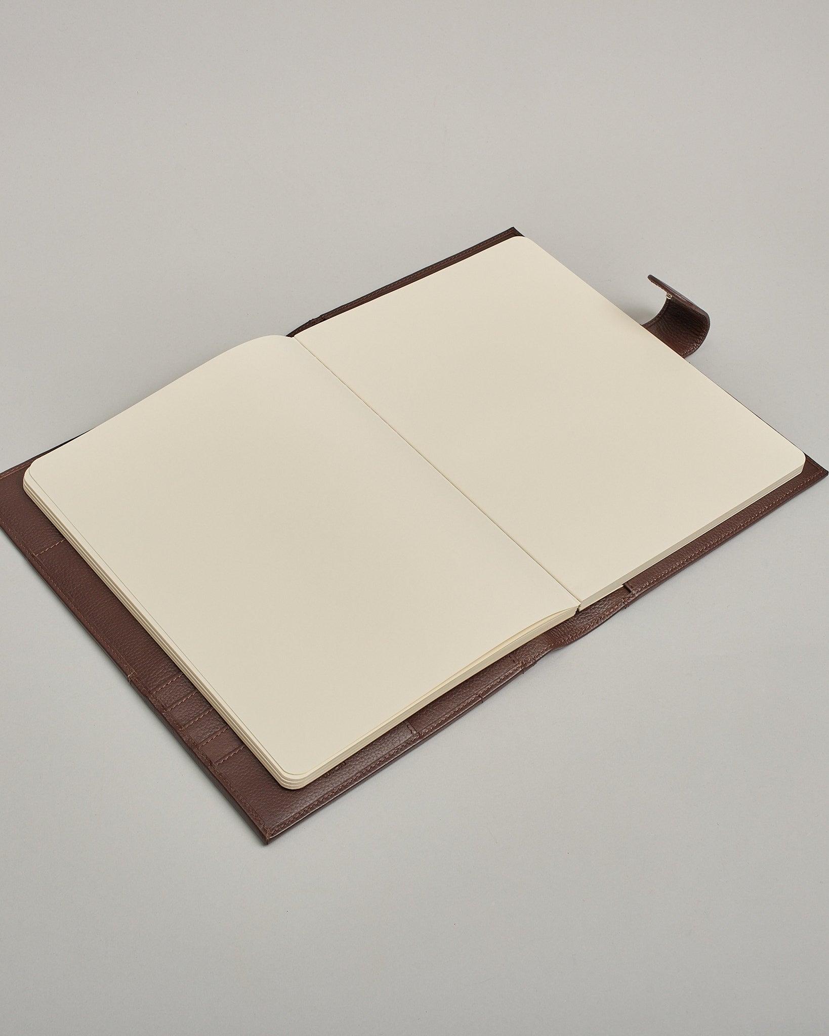 Dunkelbrauner Leder Notizbucheinband mit leichter Narbund. Der Einband hat außen ein flaches Fach in das ein Stift und das Handy gesteckt werden können. Das Notizbuch lässt sich seitlich mit einer Lasche und einem darunterliegenden Druckknopf verschließen. Innen bietet das Notizbuch rechts Platz um ein Buch einzustecken und links gibt es viele Fächer für weitere Notizzettel, Visitkarten und mehr. #6