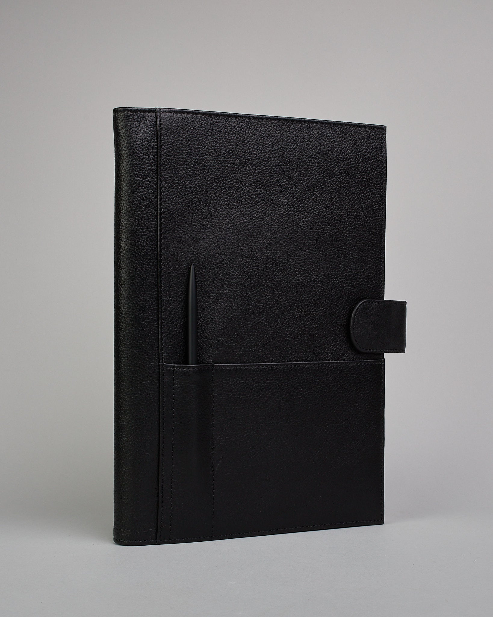 Schwarzer Leder Notizbucheinband mit leichter Narbund. Der Einband hat außen ein flaches Fach in das ein Stift und das Handy gesteckt werden können. Das Notizbuch lässt sich seitlich mit einer Lasche und einem darunterliegenden Druckknopf verschließen. Innen bietet das Notizbuch rechts Platz um ein Buch einzustecken und links gibt es viele Fächer für weitere Notizzettel, Visitkarten und mehr. #1