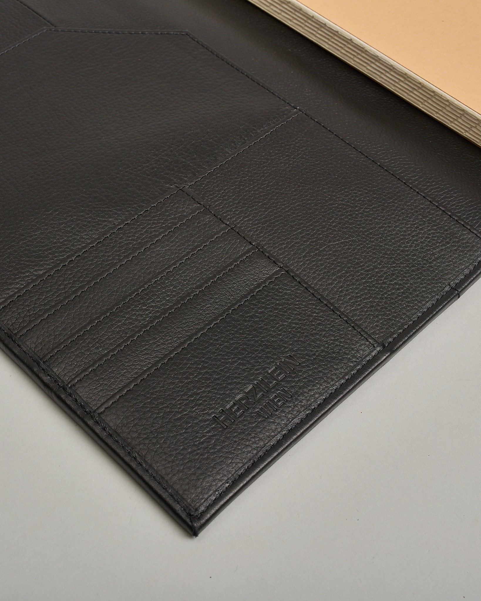 Schwarzer Leder Notizbucheinband mit leichter Narbund. Der Einband hat außen ein flaches Fach in das ein Stift und das Handy gesteckt werden können. Das Notizbuch lässt sich seitlich mit einer Lasche und einem darunterliegenden Druckknopf verschließen. Innen bietet das Notizbuch rechts Platz um ein Buch einzustecken und links gibt es viele Fächer für weitere Notizzettel, Visitkarten und mehr. #6