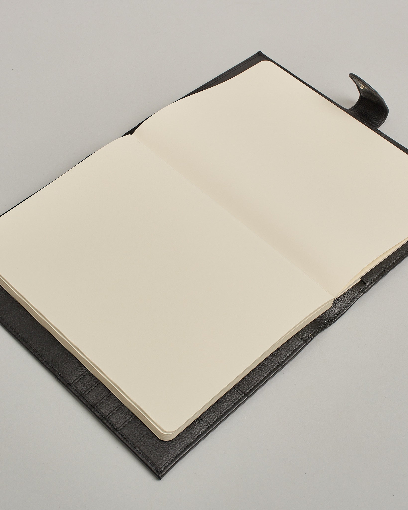 Schwarzer Leder Notizbucheinband mit leichter Narbund. Der Einband hat außen ein flaches Fach in das ein Stift und das Handy gesteckt werden können. Das Notizbuch lässt sich seitlich mit einer Lasche und einem darunterliegenden Druckknopf verschließen. Innen bietet das Notizbuch rechts Platz um ein Buch einzustecken und links gibt es viele Fächer für weitere Notizzettel, Visitkarten und mehr. #7