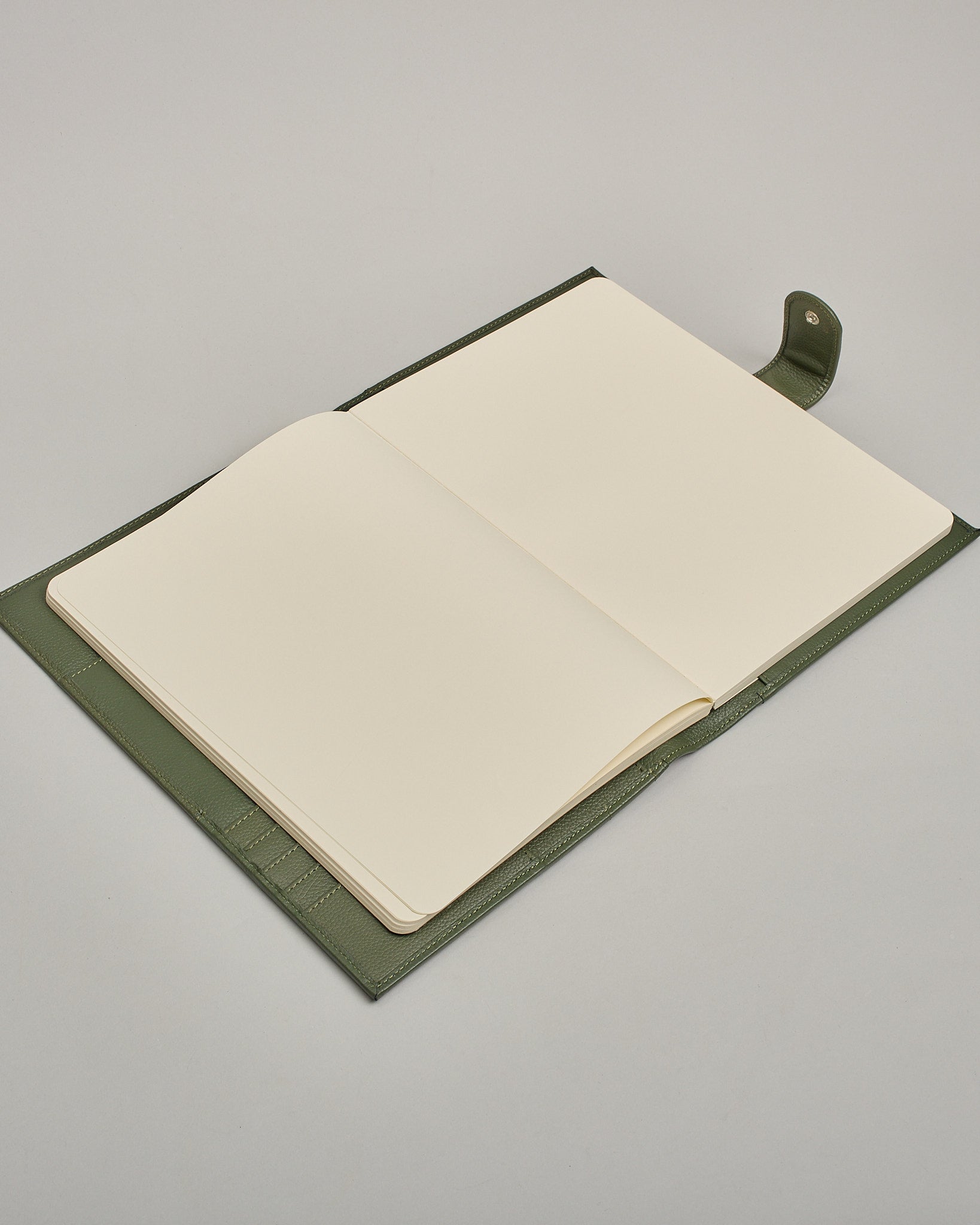 Dunkelgrüner Leder Notizbucheinband mit leichter Narbund. Der Einband hat außen ein flaches Fach in das ein Stift und das Handy gesteckt werden können. Das Notizbuch lässt sich seitlich mit einer Lasche und einem darunterliegenden Druckknopf verschließen. Innen bietet das Notizbuch rechts Platz um ein Buch einzustecken und links gibt es viele Fächer für weitere Notizzettel, Visitkarten und mehr. #7