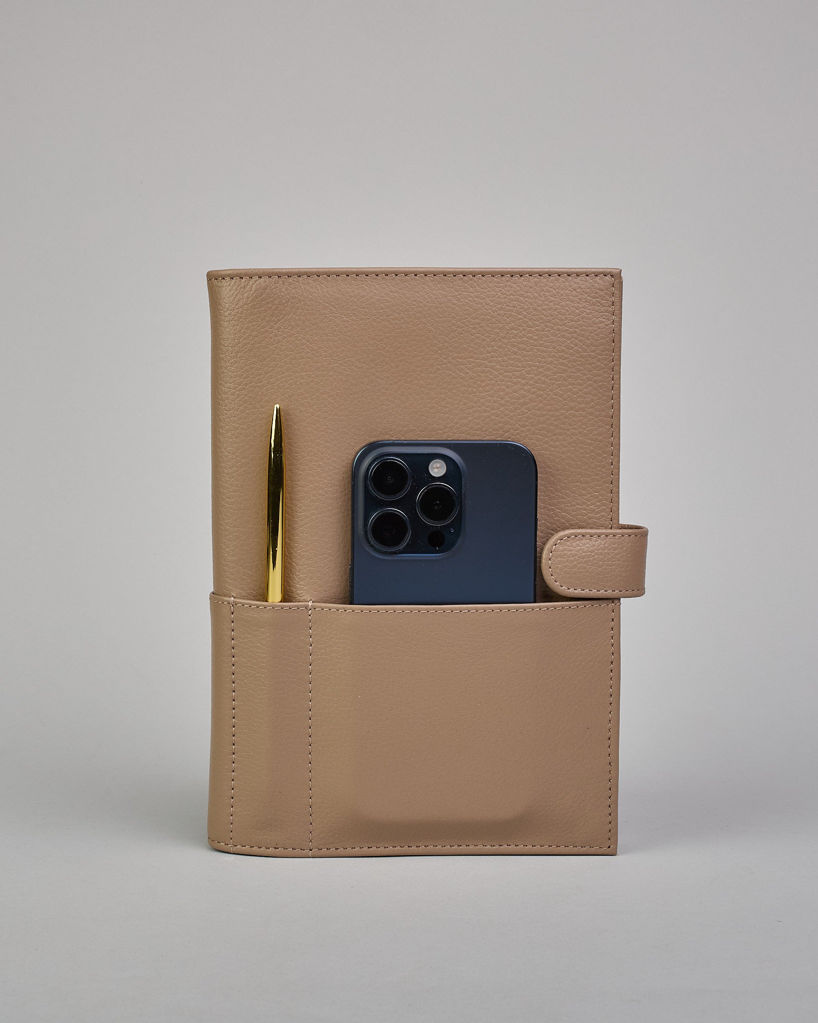 Beiger Leder Notizbucheinband mit leichter Narbund. Der Einband hat außen ein flaches Fach in das ein Stift und das Handy gesteckt werden können. Das Notizbuch lässt sich seitlich mit einer Lasche und einem darunterliegenden Druckknopf verschließen. Innen bietet das Notizbuch rechts Platz um ein Buch einzustecken und links gibt es viele Fächer für weitere Notizzettel, Visitkarten und mehr. #4