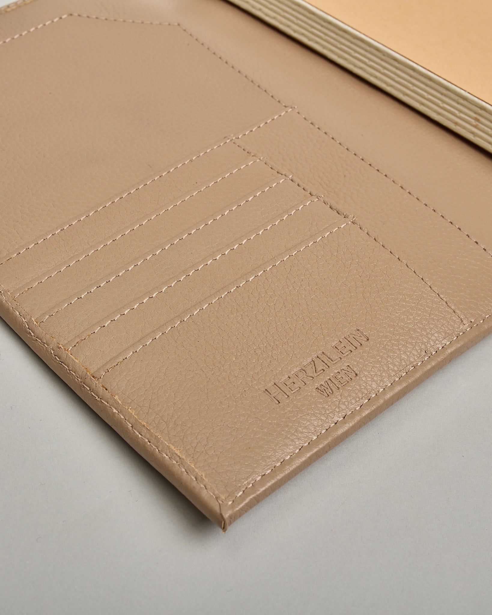 Beiger Leder Notizbucheinband mit leichter Narbund. Der Einband hat außen ein flaches Fach in das ein Stift und das Handy gesteckt werden können. Das Notizbuch lässt sich seitlich mit einer Lasche und einem darunterliegenden Druckknopf verschließen. Innen bietet das Notizbuch rechts Platz um ein Buch einzustecken und links gibt es viele Fächer für weitere Notizzettel, Visitkarten und mehr. #7