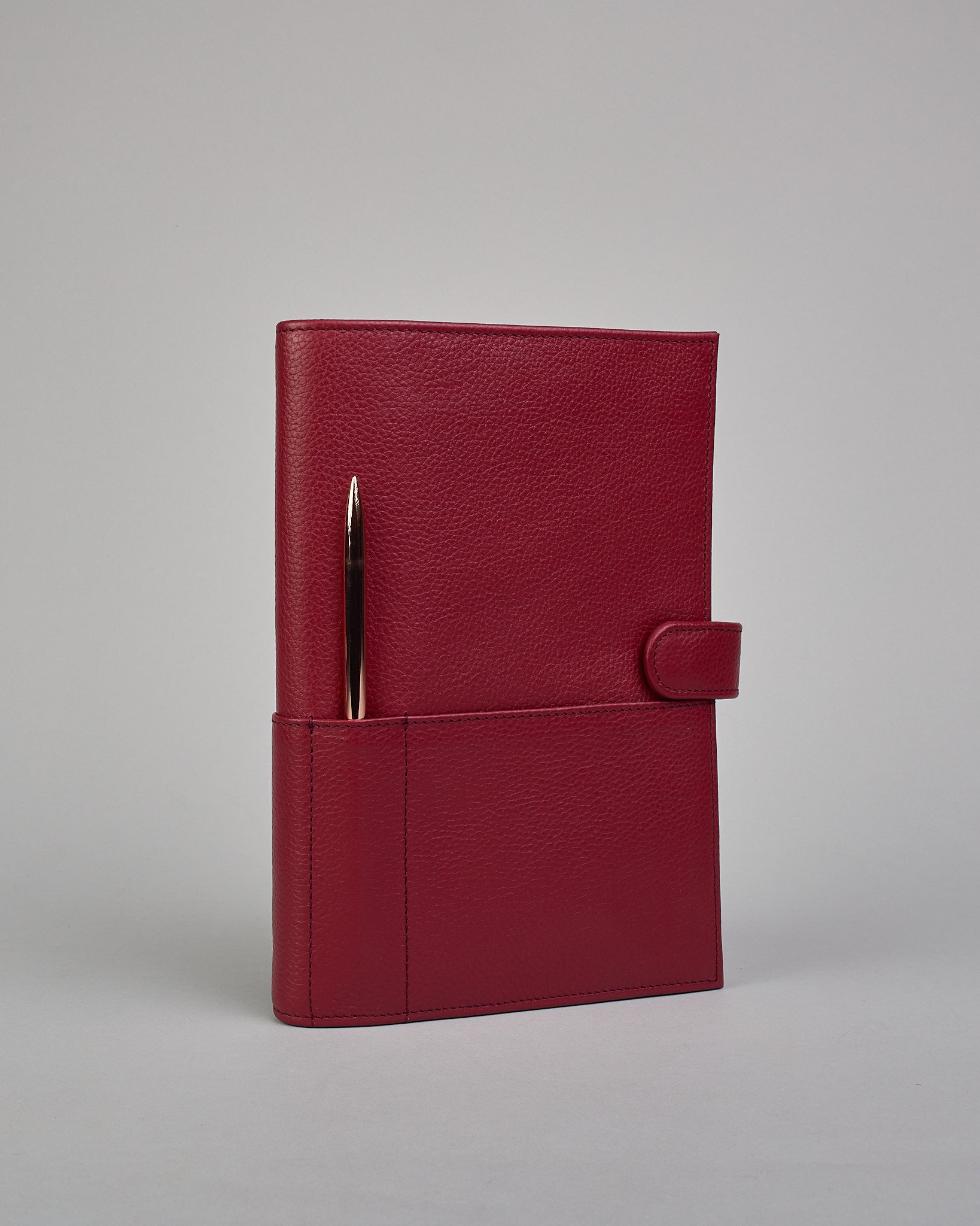 Bordeauxroter Leder Notizbucheinband mit leichter Narbund. Der Einband hat außen ein flaches Fach in das ein Stift und das Handy gesteckt werden können. Das Notizbuch lässt sich seitlich mit einer Lasche und einem darunterliegenden Druckknopf verschließen. Innen bietet das Notizbuch rechts Platz um ein Buch einzustecken und links gibt es viele Fächer für weitere Notizzettel, Visitkarten und mehr. #1