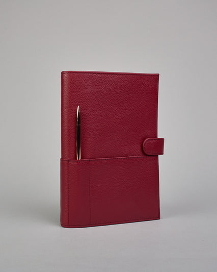 Bordeauxroter Leder Notizbucheinband mit leichter Narbund. Der Einband hat außen ein flaches Fach in das ein Stift und das Handy gesteckt werden können. Das Notizbuch lässt sich seitlich mit einer Lasche und einem darunterliegenden Druckknopf verschließen. Innen bietet das Notizbuch rechts Platz um ein Buch einzustecken und links gibt es viele Fächer für weitere Notizzettel, Visitkarten und mehr. #1