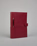 Bordeauxroter Leder Notizbucheinband mit leichter Narbund. Der Einband hat außen ein flaches Fach in das ein Stift und das Handy gesteckt werden können. Das Notizbuch lässt sich seitlich mit einer Lasche und einem darunterliegenden Druckknopf verschließen. Innen bietet das Notizbuch rechts Platz um ein Buch einzustecken und links gibt es viele Fächer für weitere Notizzettel, Visitkarten und mehr. #1