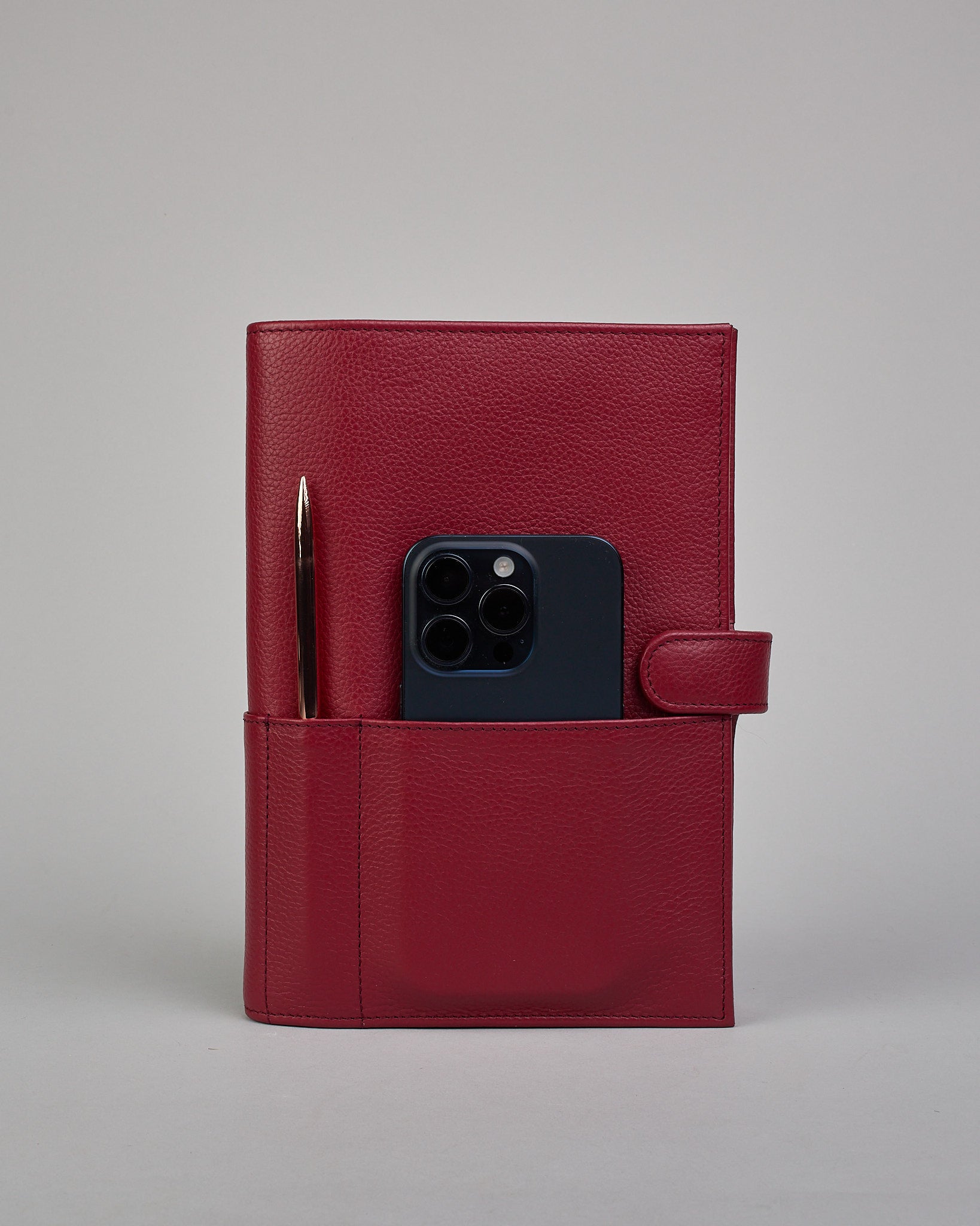 Bordeauxroter Leder Notizbucheinband mit leichter Narbund. Der Einband hat außen ein flaches Fach in das ein Stift und das Handy gesteckt werden können. Das Notizbuch lässt sich seitlich mit einer Lasche und einem darunterliegenden Druckknopf verschließen. Innen bietet das Notizbuch rechts Platz um ein Buch einzustecken und links gibt es viele Fächer für weitere Notizzettel, Visitkarten und mehr. #4