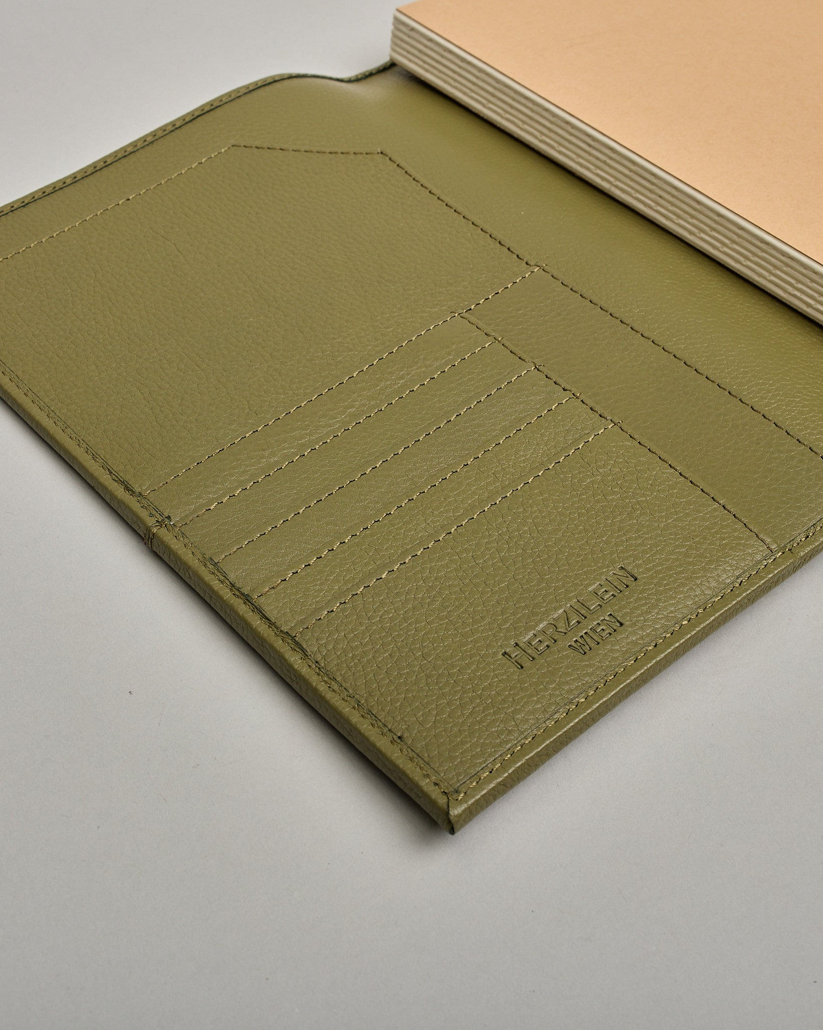 Grüner Leder Notizbucheinband mit leichter Narbund. Der Einband hat außen ein flaches Fach in das ein Stift und das Handy gesteckt werden können. Das Notizbuch lässt sich seitlich mit einer Lasche und einem darunterliegenden Druckknopf verschließen. Innen bietet das Notizbuch rechts Platz um ein Buch einzustecken und links gibt es viele Fächer für weitere Notizzettel, Visitkarten und mehr. #6