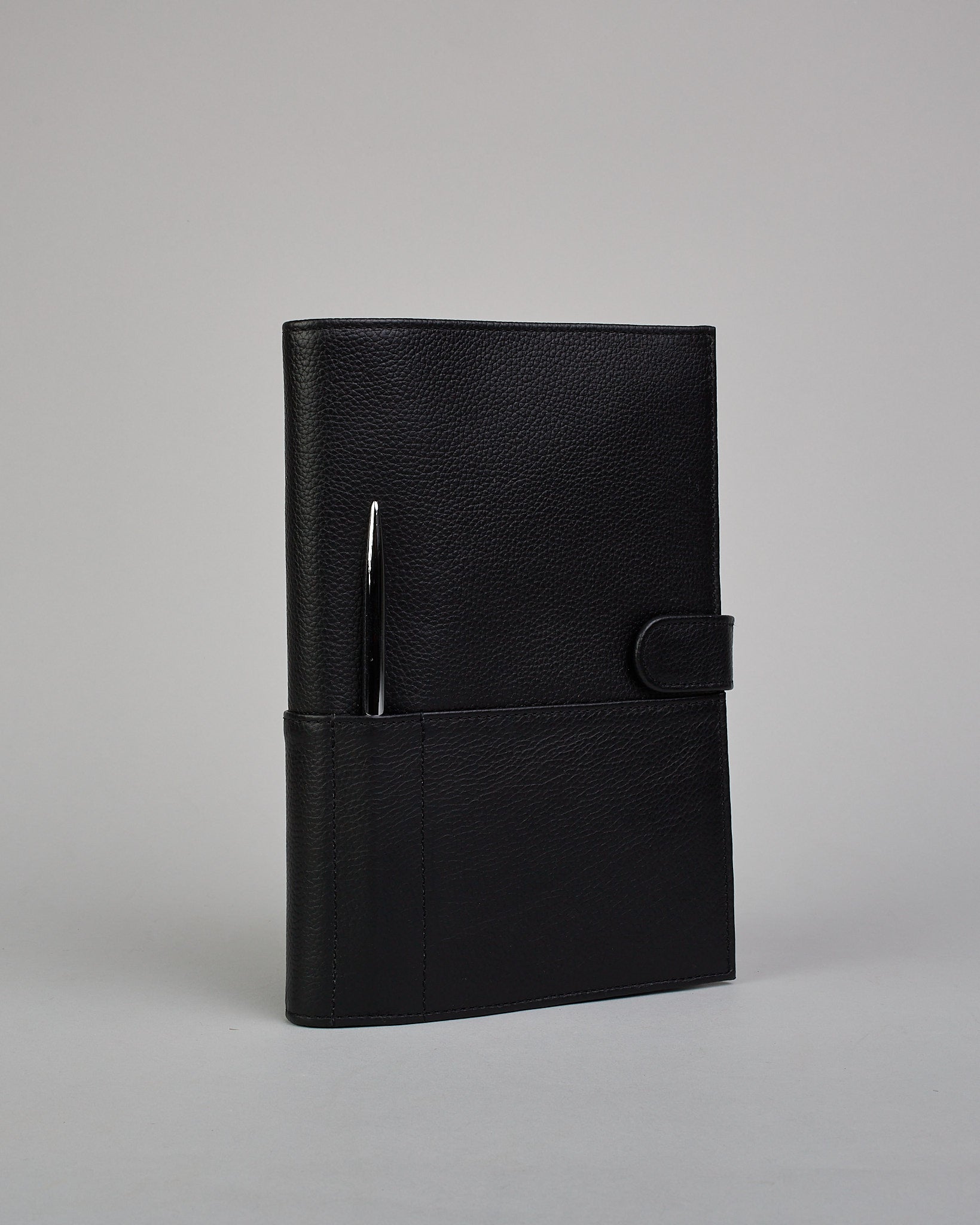 Schwarzer Leder Notizbucheinband mit leichter Narbund. Der Einband hat außen ein flaches Fach in das ein Stift und das Handy gesteckt werden können. Das Notizbuch lässt sich seitlich mit einer Lasche und einem darunterliegenden Druckknopf verschließen. Innen bietet das Notizbuch rechts Platz um ein Buch einzustecken und links gibt es viele Fächer für weitere Notizzettel, Visitkarten und mehr. #1