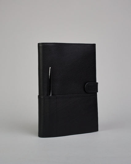 Schwarzer Leder Notizbucheinband mit leichter Narbund. Der Einband hat außen ein flaches Fach in das ein Stift und das Handy gesteckt werden können. Das Notizbuch lässt sich seitlich mit einer Lasche und einem darunterliegenden Druckknopf verschließen. Innen bietet das Notizbuch rechts Platz um ein Buch einzustecken und links gibt es viele Fächer für weitere Notizzettel, Visitkarten und mehr. #1