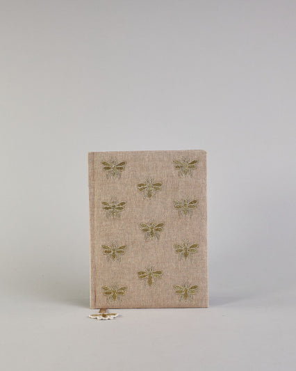 Beiges Notizbuch mti Baumwolleinband und vielen gestickten goldenen Bienen in regelmäßigen Abständen auf dem Einband. Lesezeichen mit goldener Biene als Anhänger. Linierte Seiten innen. #1