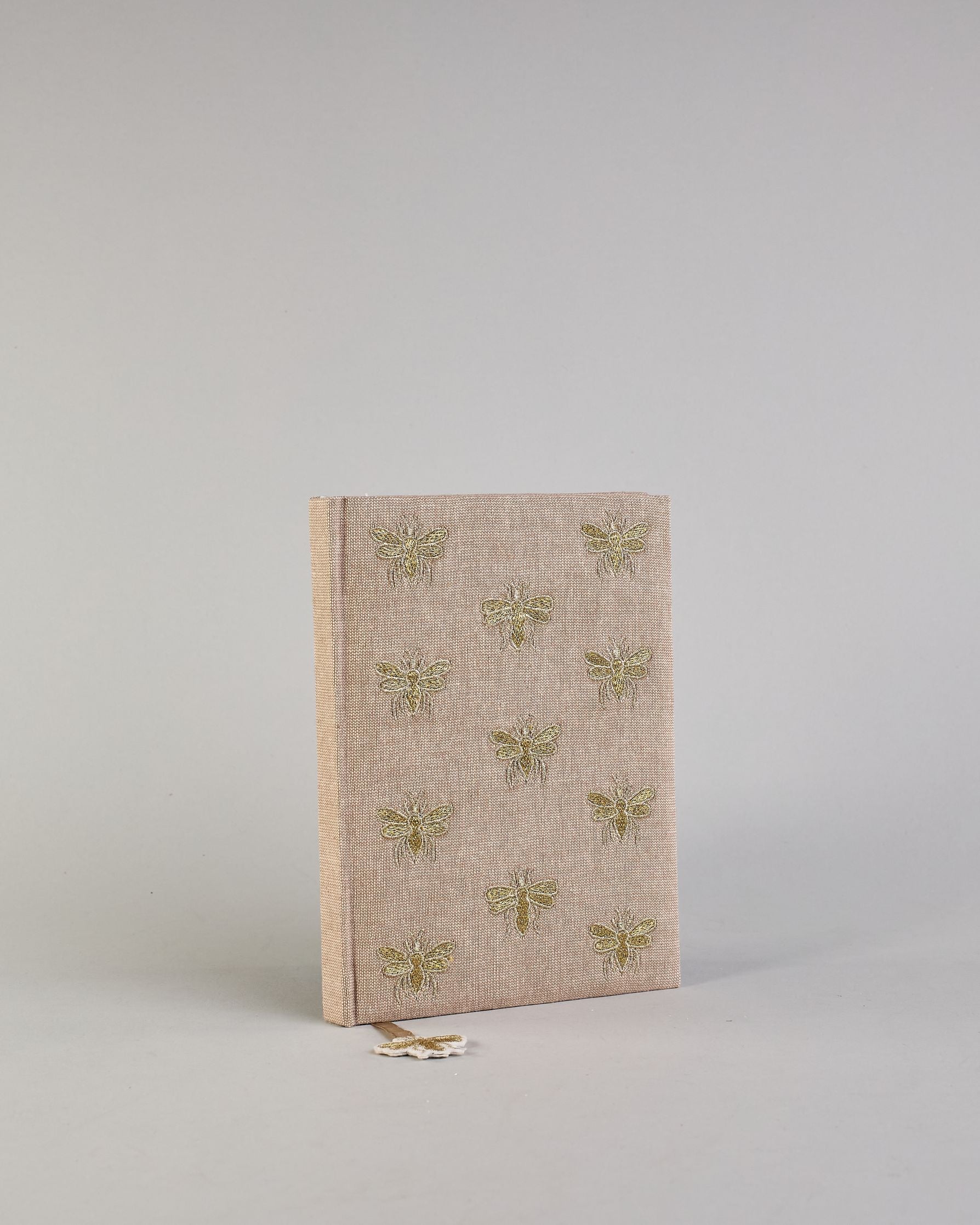 Beiges Notizbuch mti Baumwolleinband und vielen gestickten goldenen Bienen in regelmäßigen Abständen auf dem Einband. Lesezeichen mit goldener Biene als Anhänger. Linierte Seiten innen. #2