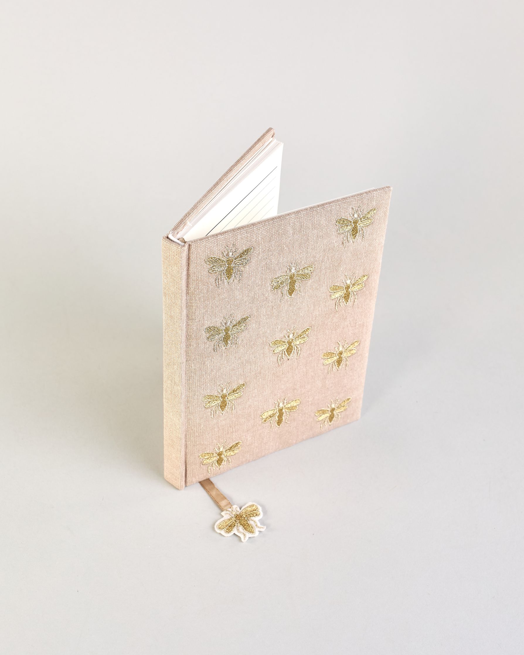 Beiges Notizbuch mti Baumwolleinband und vielen gestickten goldenen Bienen in regelmäßigen Abständen auf dem Einband. Lesezeichen mit goldener Biene als Anhänger. Linierte Seiten innen. #3
