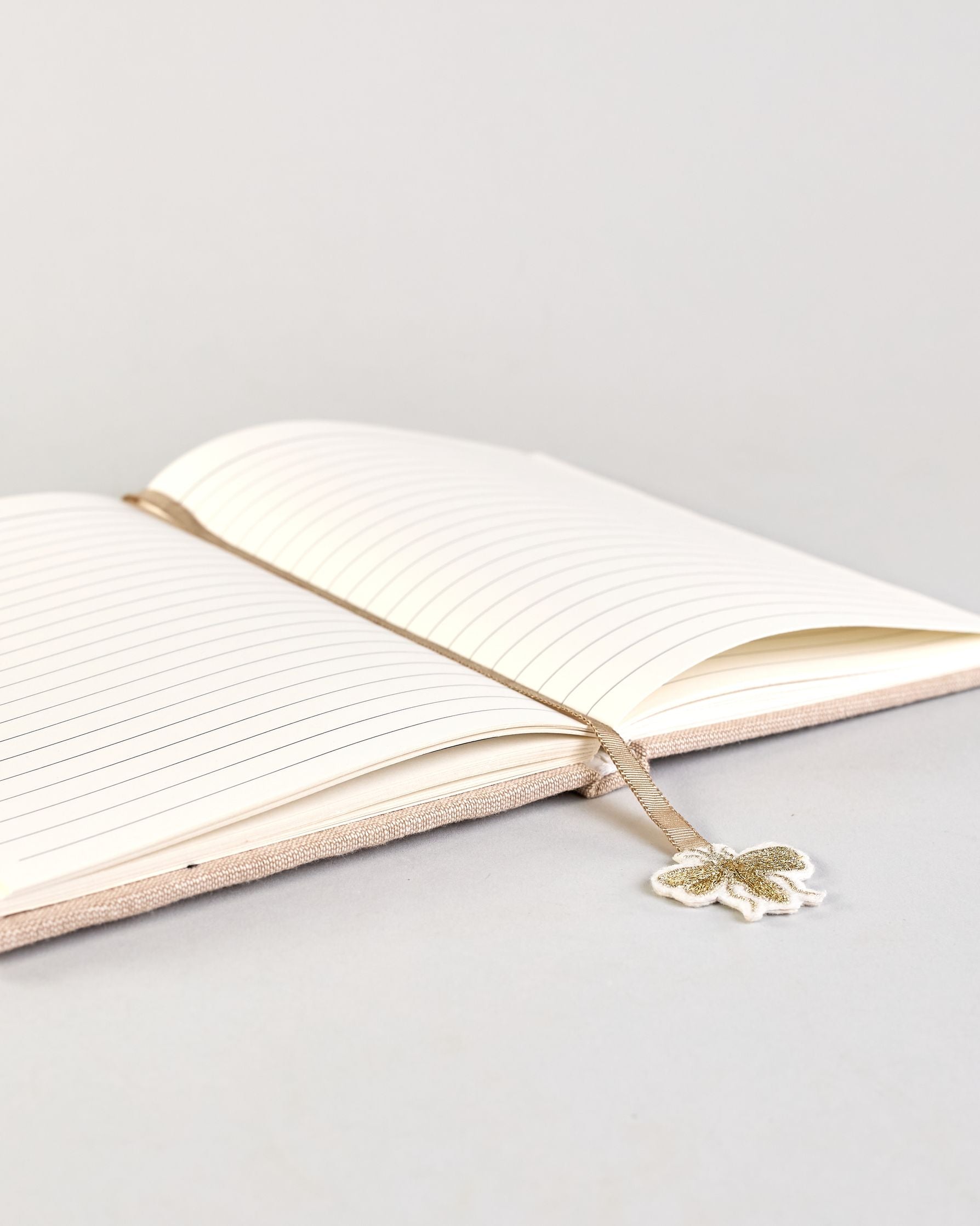 Beiges Notizbuch mti Baumwolleinband und vielen gestickten goldenen Bienen in regelmäßigen Abständen auf dem Einband. Lesezeichen mit goldener Biene als Anhänger. Linierte Seiten innen. #4