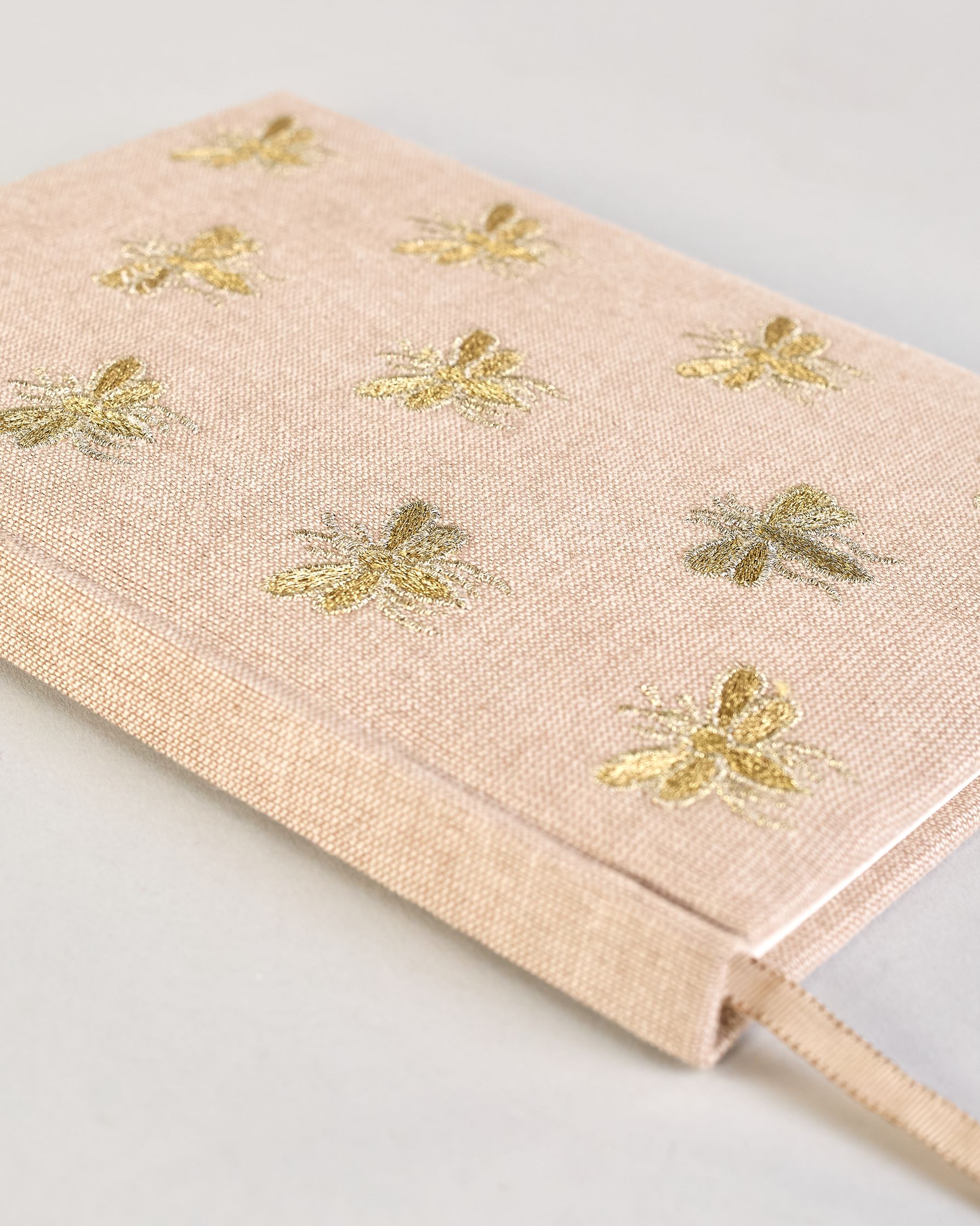 Beiges Notizbuch mti Baumwolleinband und vielen gestickten goldenen Bienen in regelmäßigen Abständen auf dem Einband. Lesezeichen mit goldener Biene als Anhänger. Linierte Seiten innen. #6