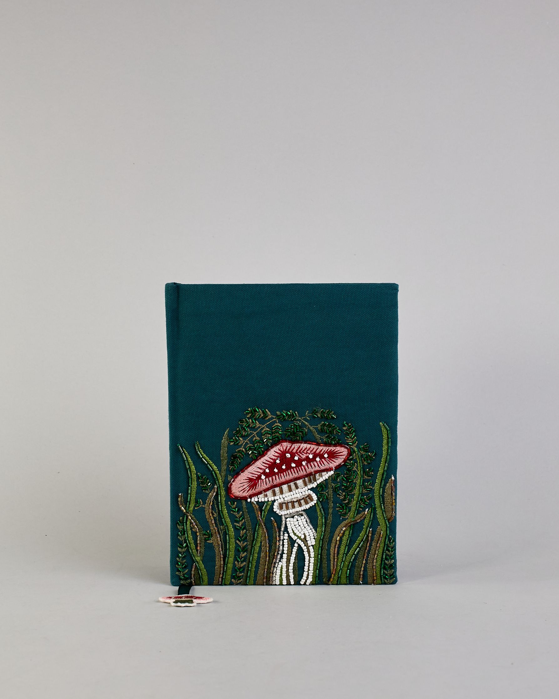 Petrolfarbenes Notizbuch mit Baumwolleinband und großem Fliegenpilz aus Perlen gestickt auf den Bucheinband, runderherum ist noch Gras aus Perlen. Lesezeichen mit Fliegenpilz als Anähnger. Linierte Seiten #1
