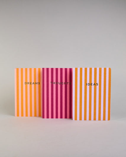 Set aus drei A5-Heften mit recyceltem Baumwolleinband. Die Hefte sind mit senkrechten Streifen in Blau- und Grüntönen gestaltet und zeigen auf dem Cover jeweils ein goldener Spruch: Dreams, Thoughts und Ideas. 30 linierte Seiten innen. #1