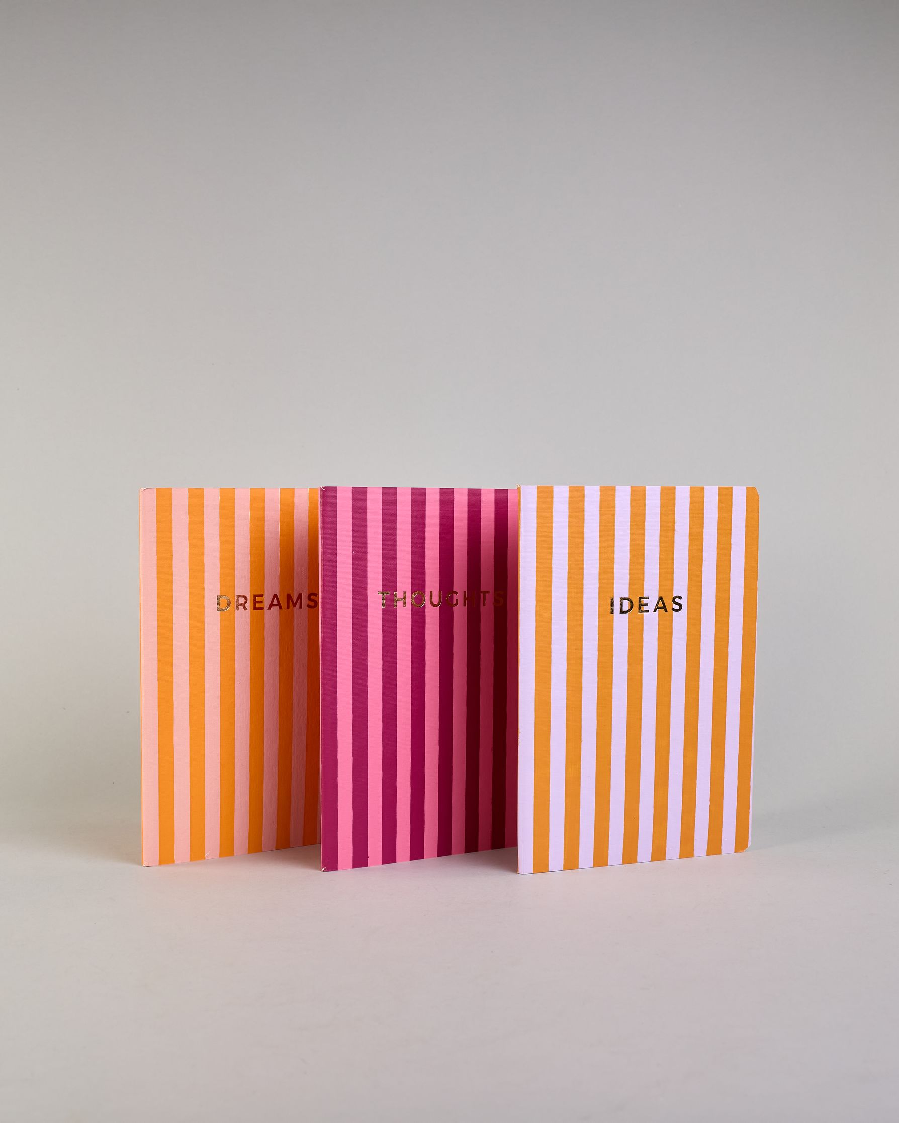 Set aus drei A5-Heften mit recyceltem Baumwolleinband. Die Hefte sind mit senkrechten Streifen in Blau- und Grüntönen gestaltet und zeigen auf dem Cover jeweils ein goldener Spruch: Dreams, Thoughts und Ideas. 30 linierte Seiten innen. #2