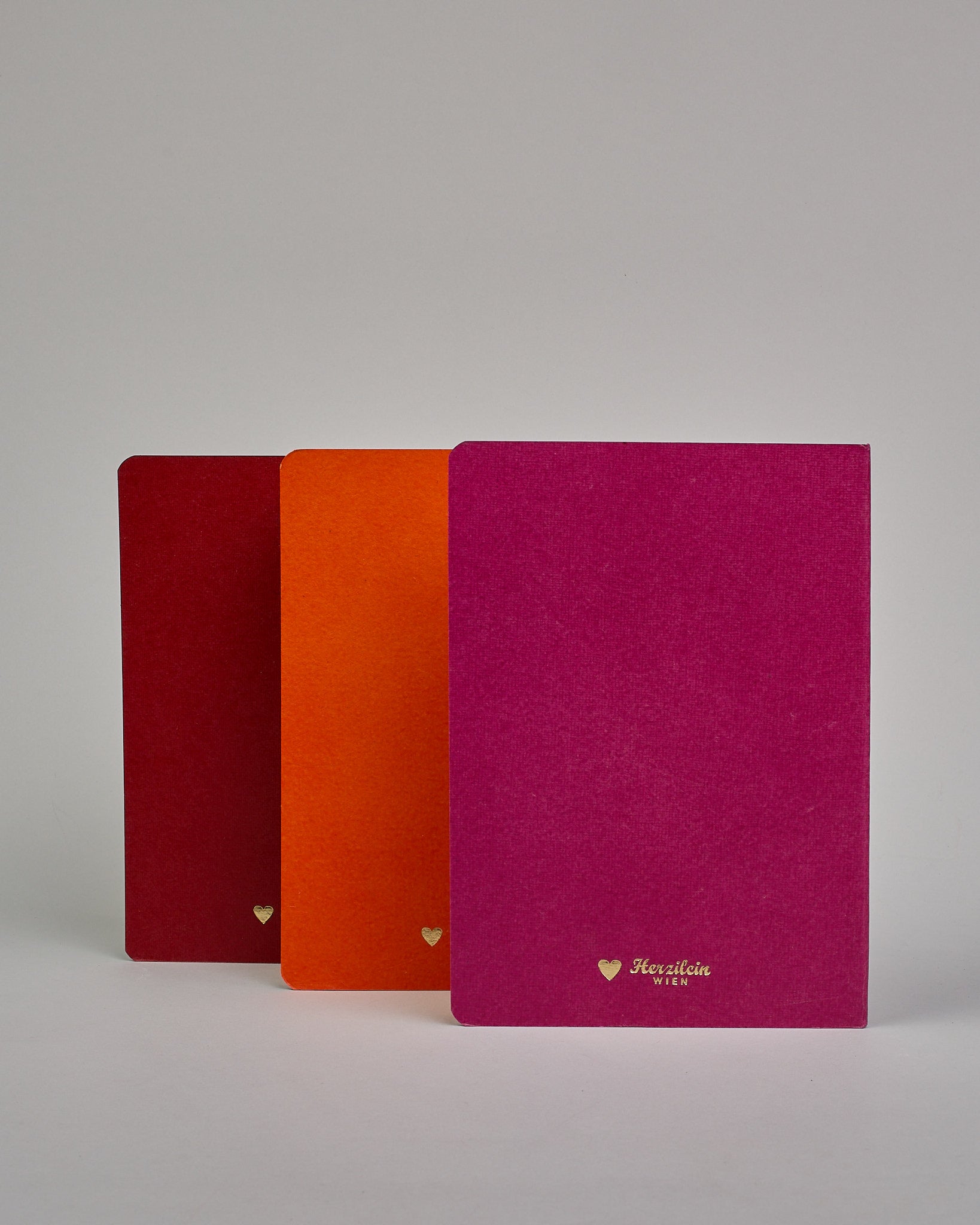 Set bestehend aus drei Heften in magenta, dunkelrot und orange. Jedes hat eine andere Prägung oben Mittig in gold. Das magentafarbene eine Pfingstrose, das dunkelrote einen Zweig mit Blumen, das orangene ein vollflächiges Blumenmuster. Innen sind sie glatt. #2