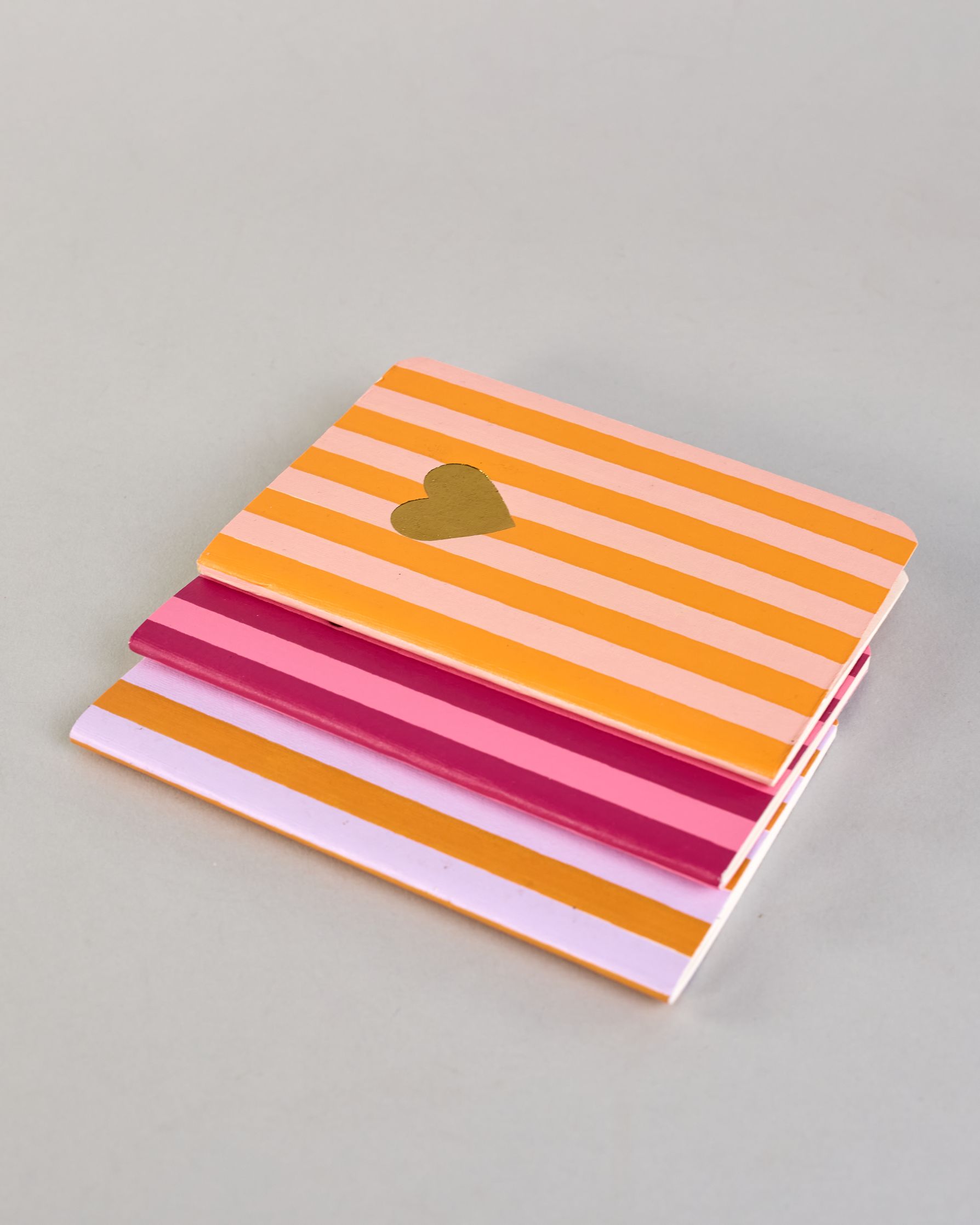 Set aus drei A6-Heften mit recyceltem Baumwolleinband. Die Hefte sind mit senkrechten Streifen in Blau- und Grüntönen gestaltet und zeigen auf dem Cover jeweils ein goldenes Motiv: ein Herz, ein Kleeblatt und eine Libelle. 30 glatte Seiten innen. #11