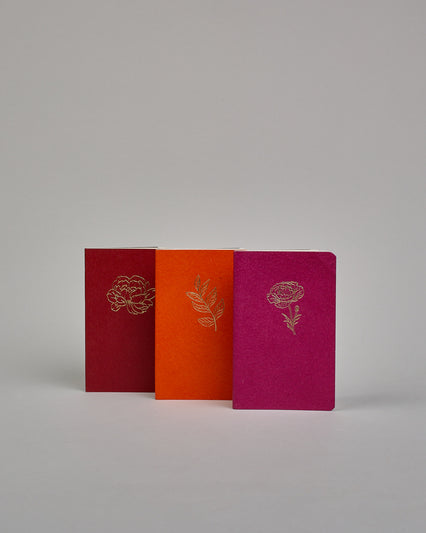 Set bestehend aus drei Heften in magenta, dunkelrot und orange. Jedes hat eine andere Prägung oben Mittig in gold. Das magentafarbene eine Pfingstrose, das dunkelrote eine Rose, das orangene einen Zweig mit Blättern. Innen sind sie glatt. #1