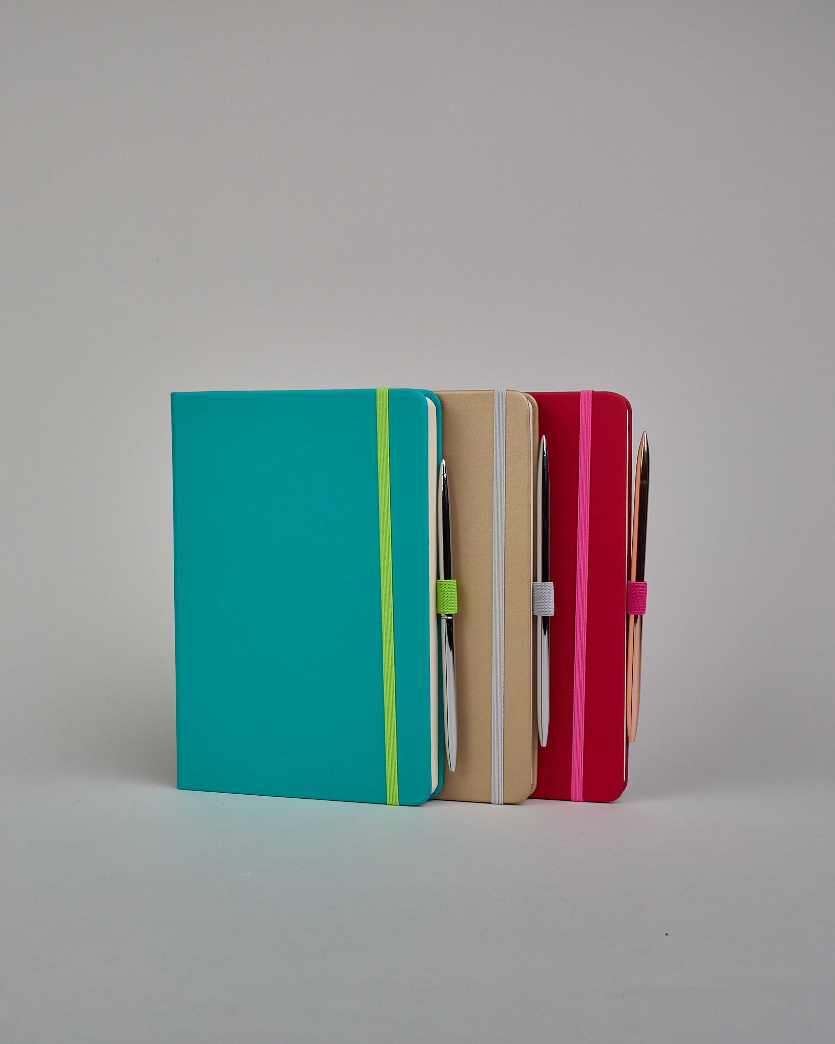 Dunkelrotes Notizbuch mit Soft-Touch Einband, pinkem Gummi zum Verschließen und Lasche aus dem selben Gummi zum Einstecken von einem Stift auf der rechten Seite. Innen finden sich 190 gepunktete Seiten mit Seitennummerierung.