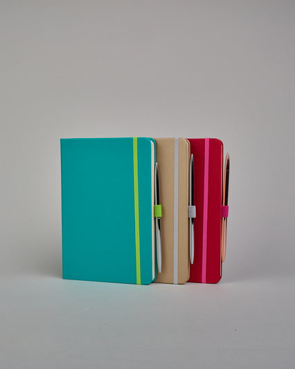 Dunkelrotes Notizbuch mit Soft-Touch Einband, pinkem Gummi zum Verschließen und Lasche aus dem selben Gummi zum Einstecken von einem Stift auf der rechten Seite. Innen finden sich 190 gepunktete Seiten mit Seitennummerierung.