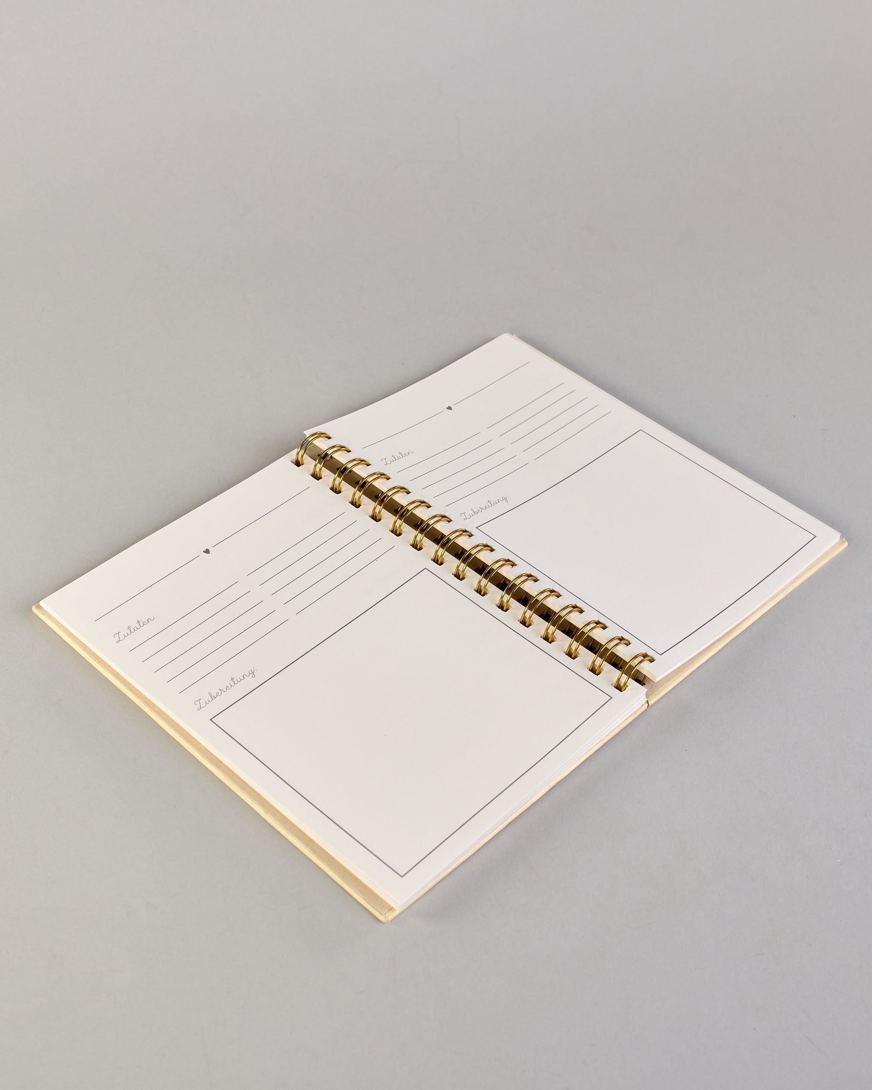 Spiralgebundenes Rezeptbuch mit goldfarbener Wire-O-Bindung und festem cremefarbenem Baumwolleinband aus recycelter Baumwolle. Der Einband ist mit schwarzen Illustrationen von Küchenutensilien wie Schneebesen, Kochlöffel, Messer, Töpfen, Schneidebrett, Pfanne und Sieb dekoriert. Auf den cremeweißen Innenseiten sind vorgedruckte Linien und Felder für das Eintragen von Zutaten und Zubereitungsschritten vorgesehen, jeweils mit klar abgetrennten Bereichen. #3