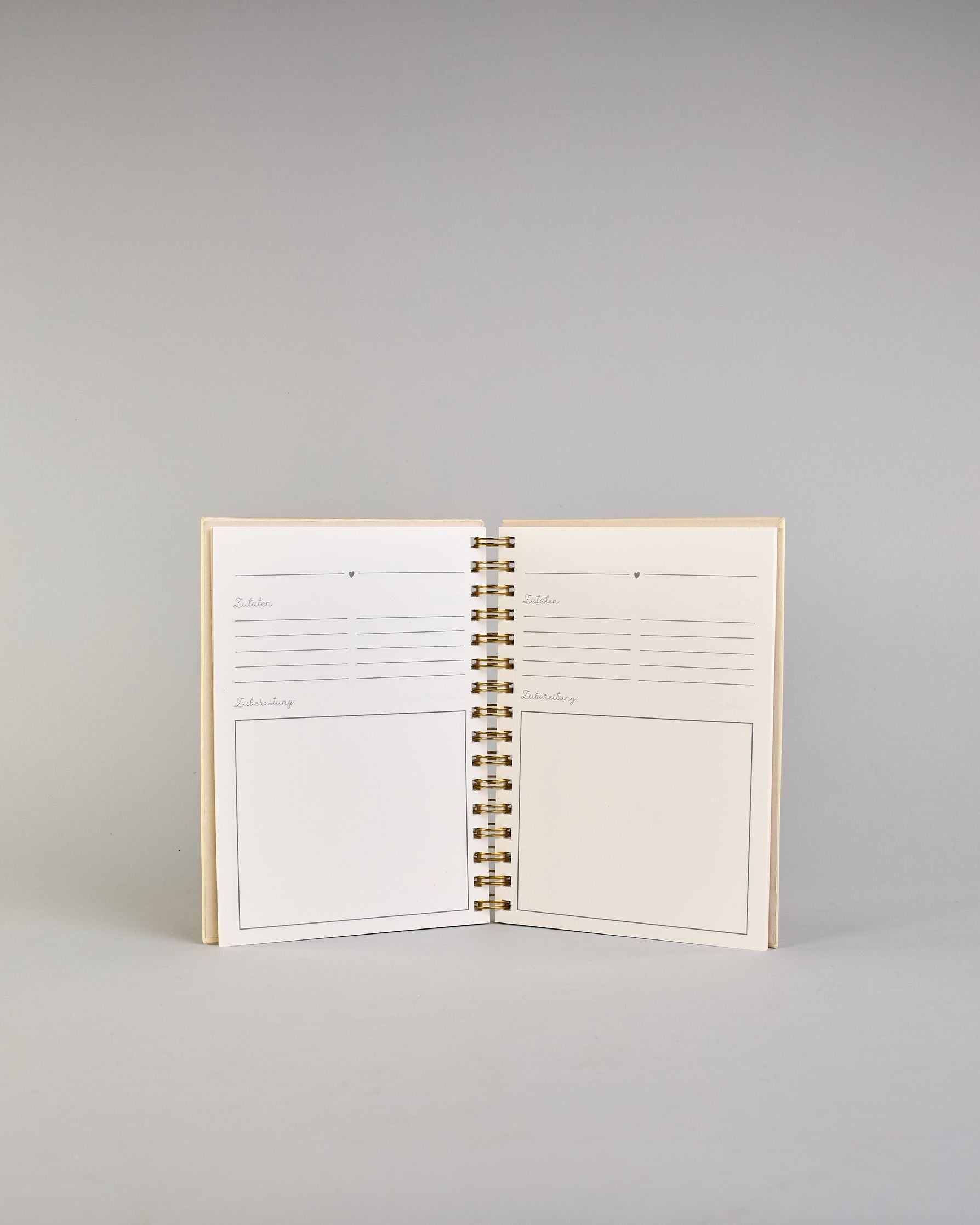 Spiralgebundenes Rezeptbuch mit goldfarbener Wire-O-Bindung und festem cremefarbenem Baumwolleinband aus recycelter Baumwolle. Der Einband ist mit schwarzen Illustrationen von Küchenutensilien wie Schneebesen, Kochlöffel, Messer, Töpfen, Schneidebrett, Pfanne und Sieb dekoriert. Auf den cremeweißen Innenseiten sind vorgedruckte Linien und Felder für das Eintragen von Zutaten und Zubereitungsschritten vorgesehen, jeweils mit klar abgetrennten Bereichen. #6