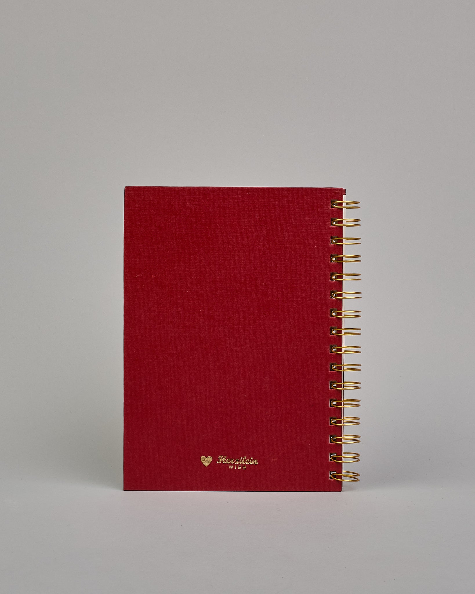 Spiral-Kochbuch mit goldender Spiralbindung, das Cover ist dunkelrot und hat eine goldene Prägung die eine Leine darstellt auf der verschiedene Kochlöffel hängen, darunter steht ebenso in gold geprägt Rezepte #2